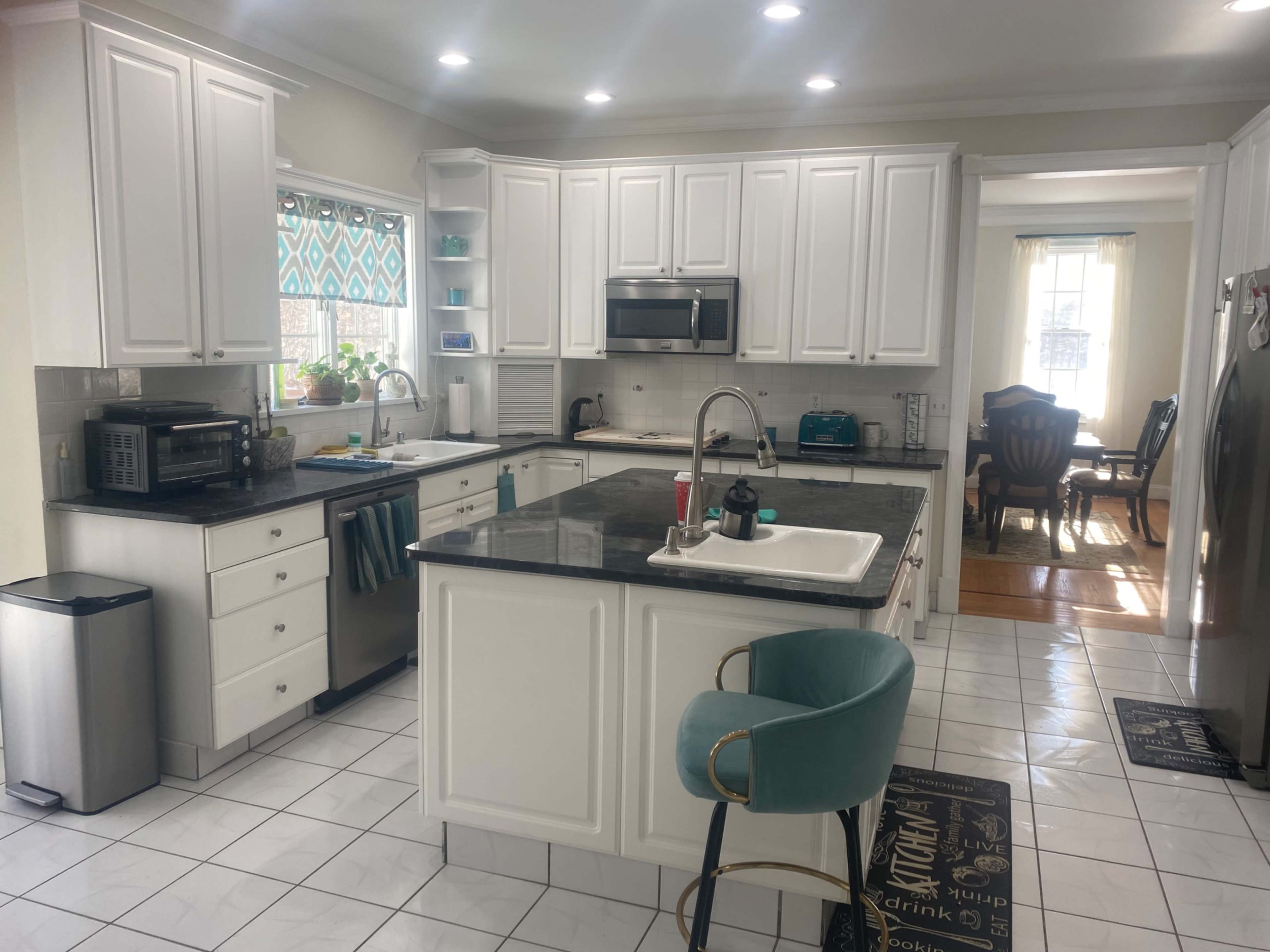 The image shows a modern kitchen with white cabinetry, a black countertop, and a dining area visible through an open layout.