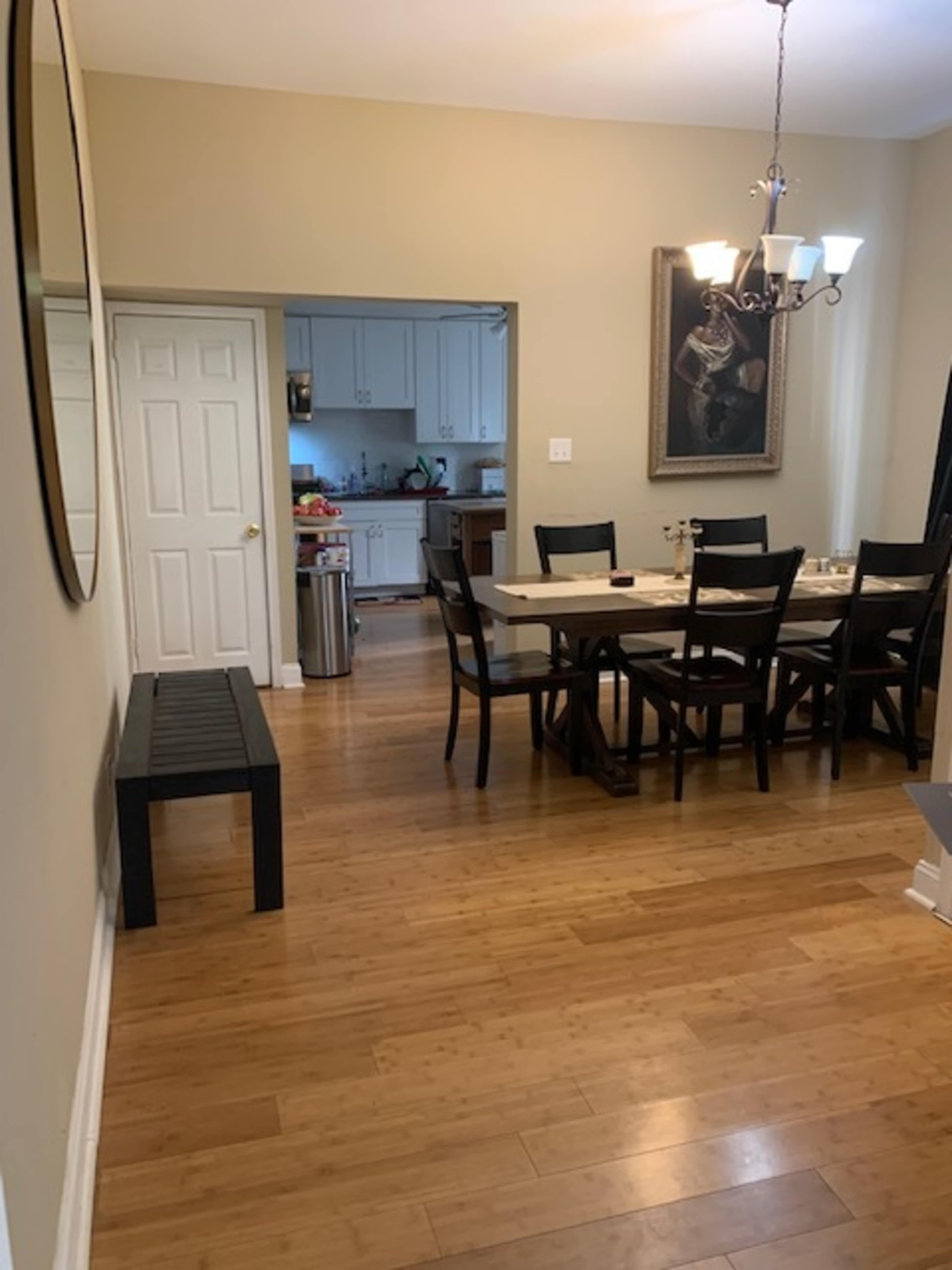 A dining area with a long table and chairs, leading to an adjacent kitchen visible through an open door.