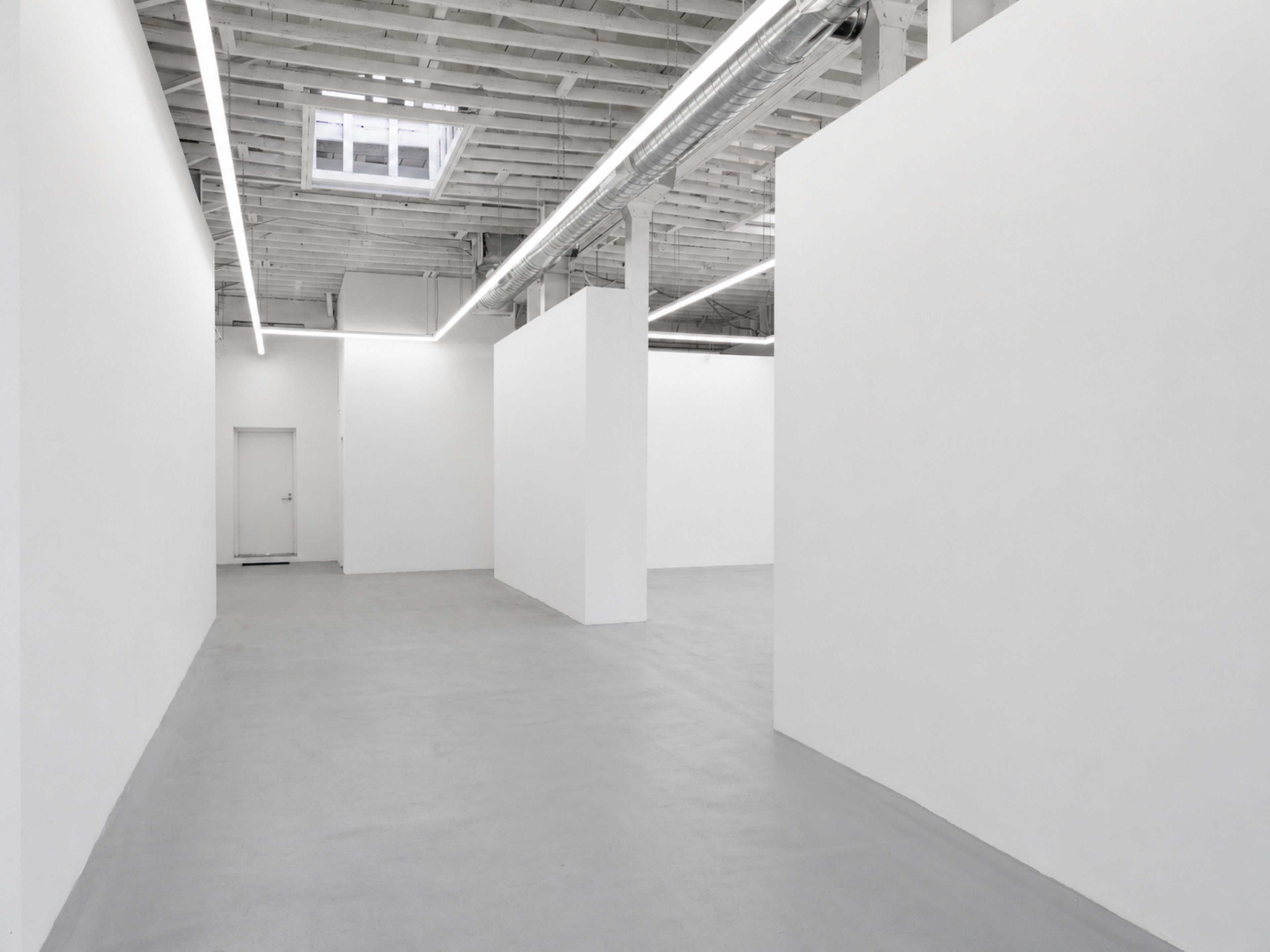 The image shows an empty, minimalist interior of a gallery with white walls and a concrete floor.