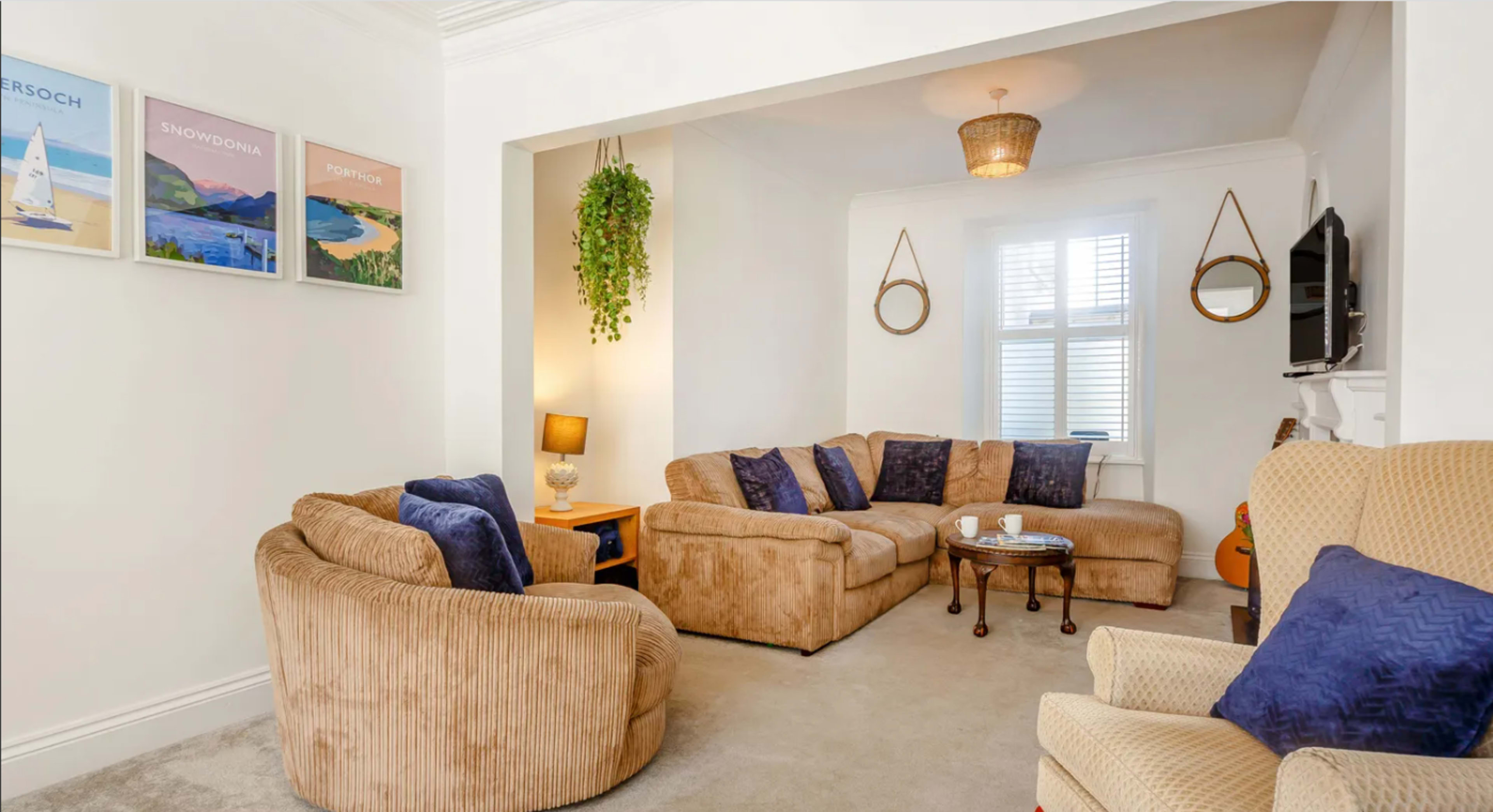 A living room with a large beige sectional sofa, a couple of armchairs, a coffee table, and wall art featuring landscapes.