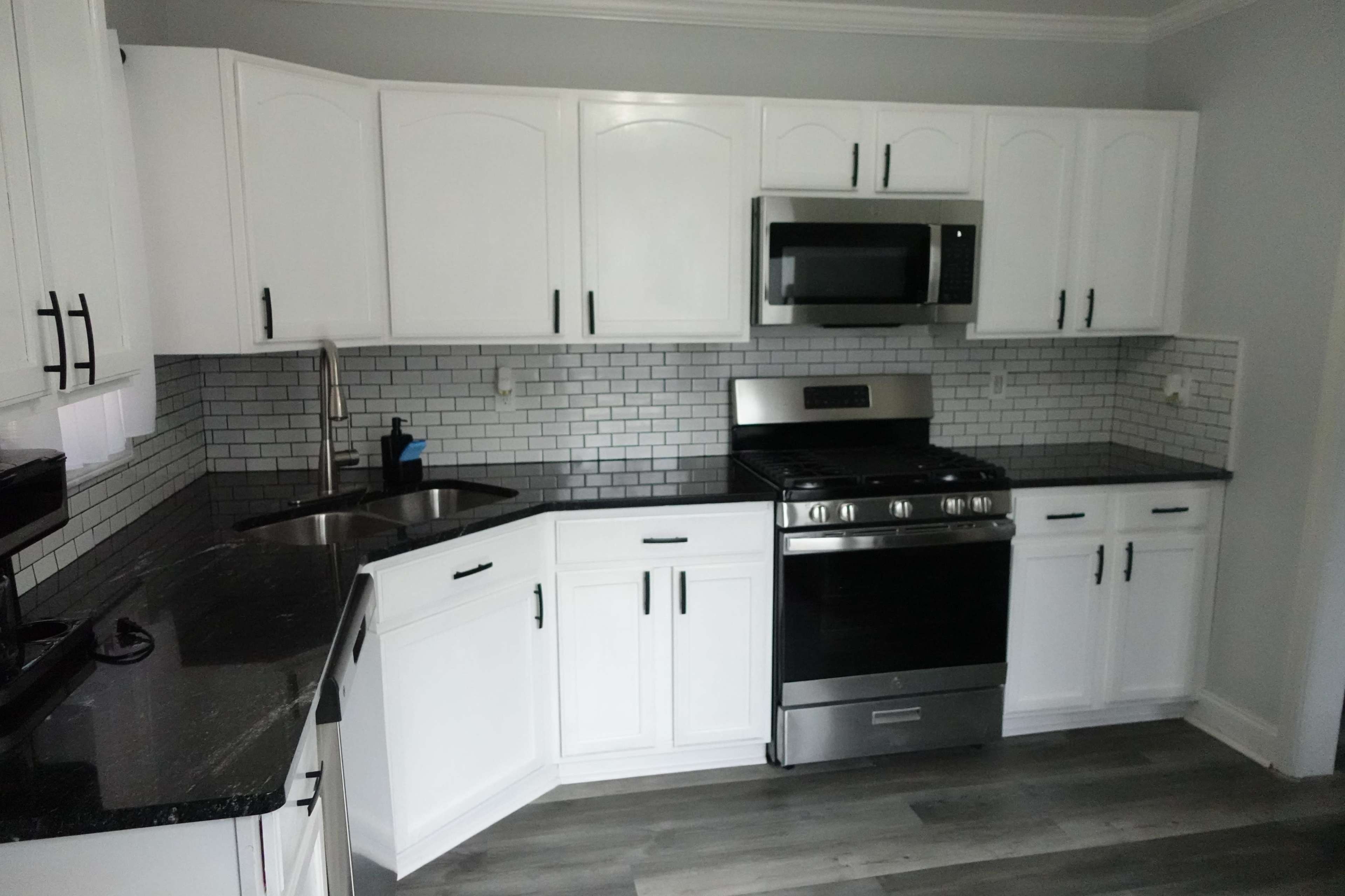 A kitchen with white cabinets, stainless steel appliances, and black countertops with a tiled backsplash.