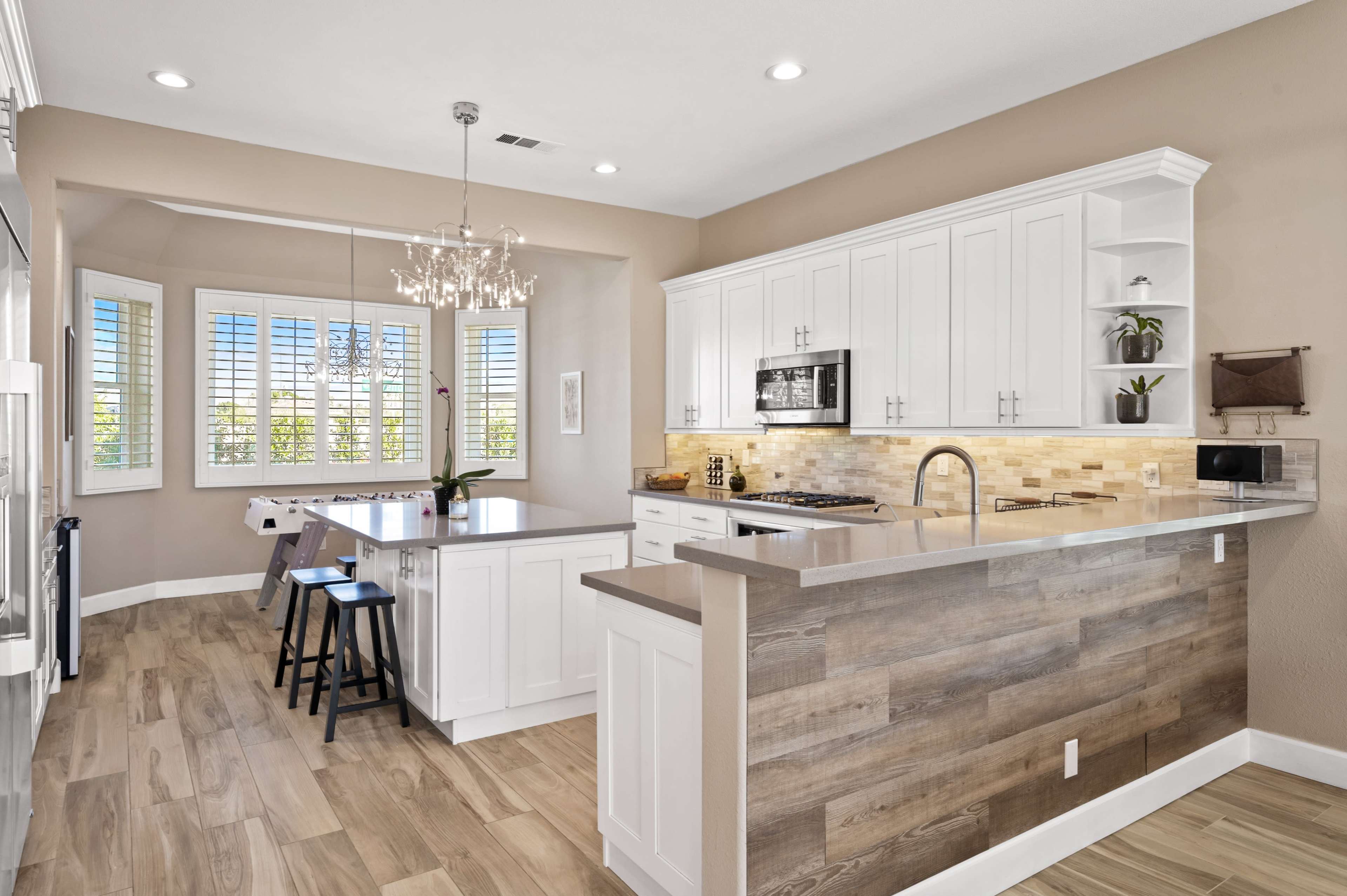 The image shows a modern kitchen with white cabinets, a central island, and large windows overlooking a patio area.