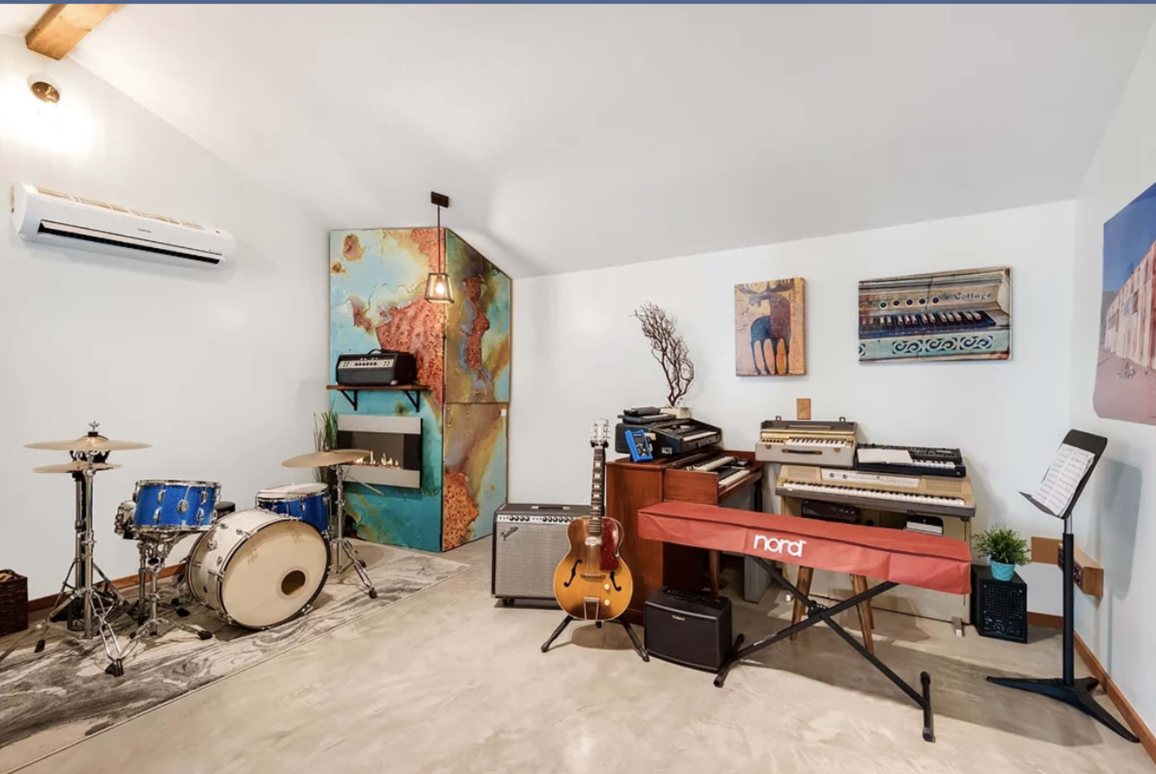 The image features a music studio with a drum set, various musical instruments, and colorful wall art.