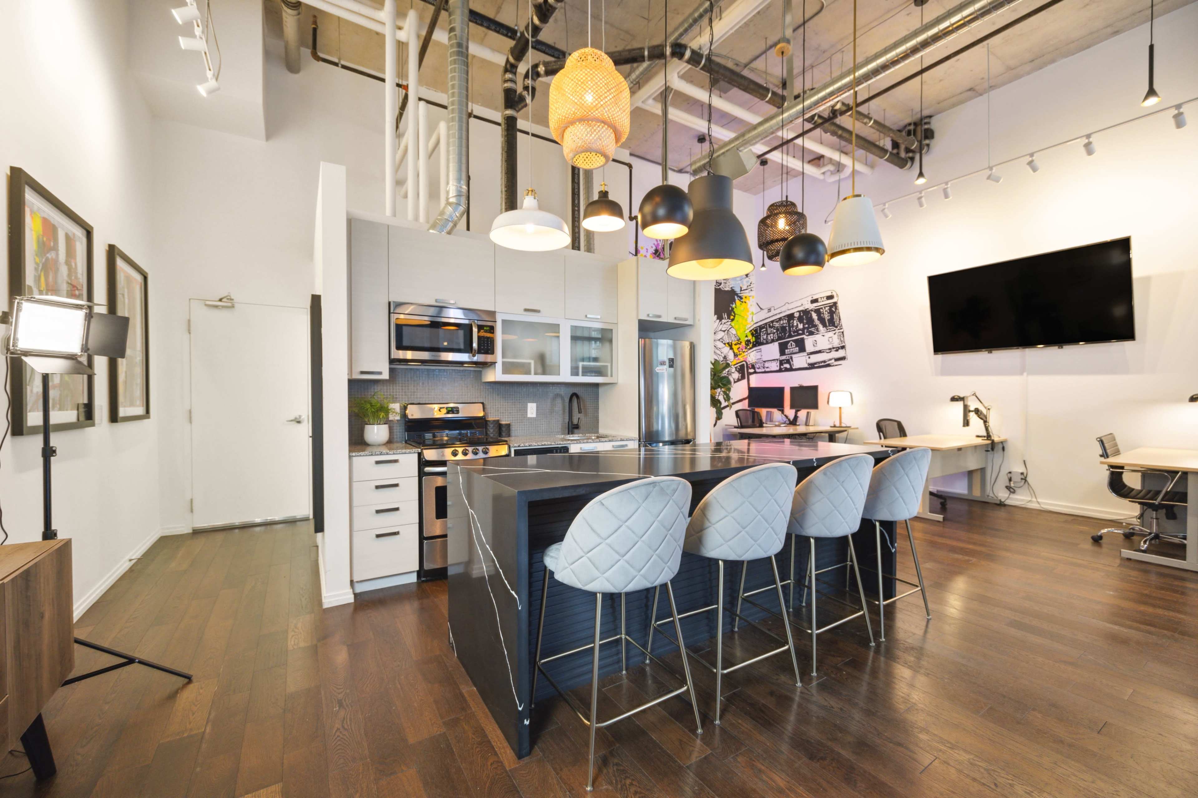 A modern kitchen features an island with bar seating, stainless steel appliances, and pendant lighting in a spacious, industrial-style room.