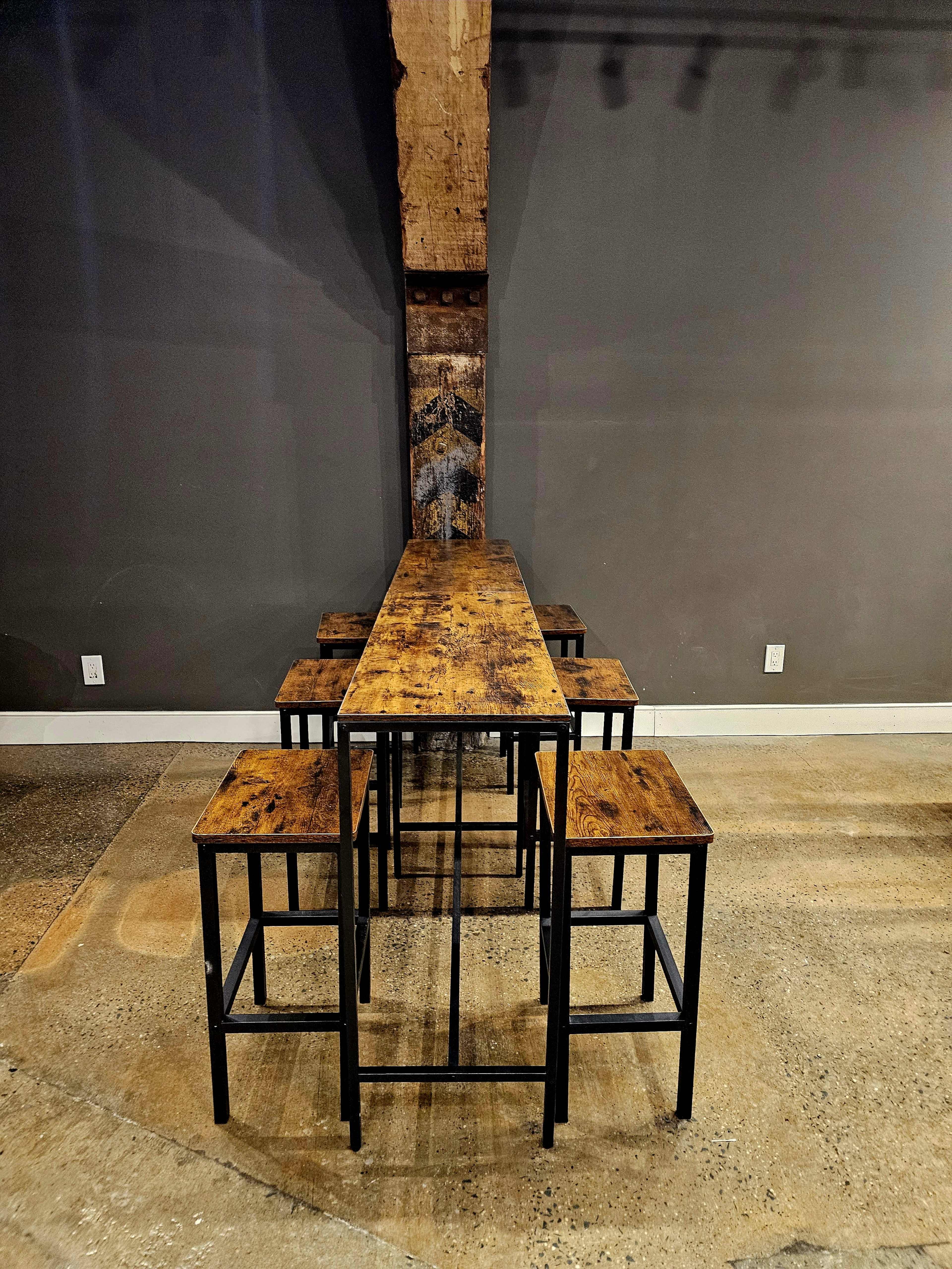 A long wooden table with metal legs is set against a gray wall, accompanied by four matching stools.
