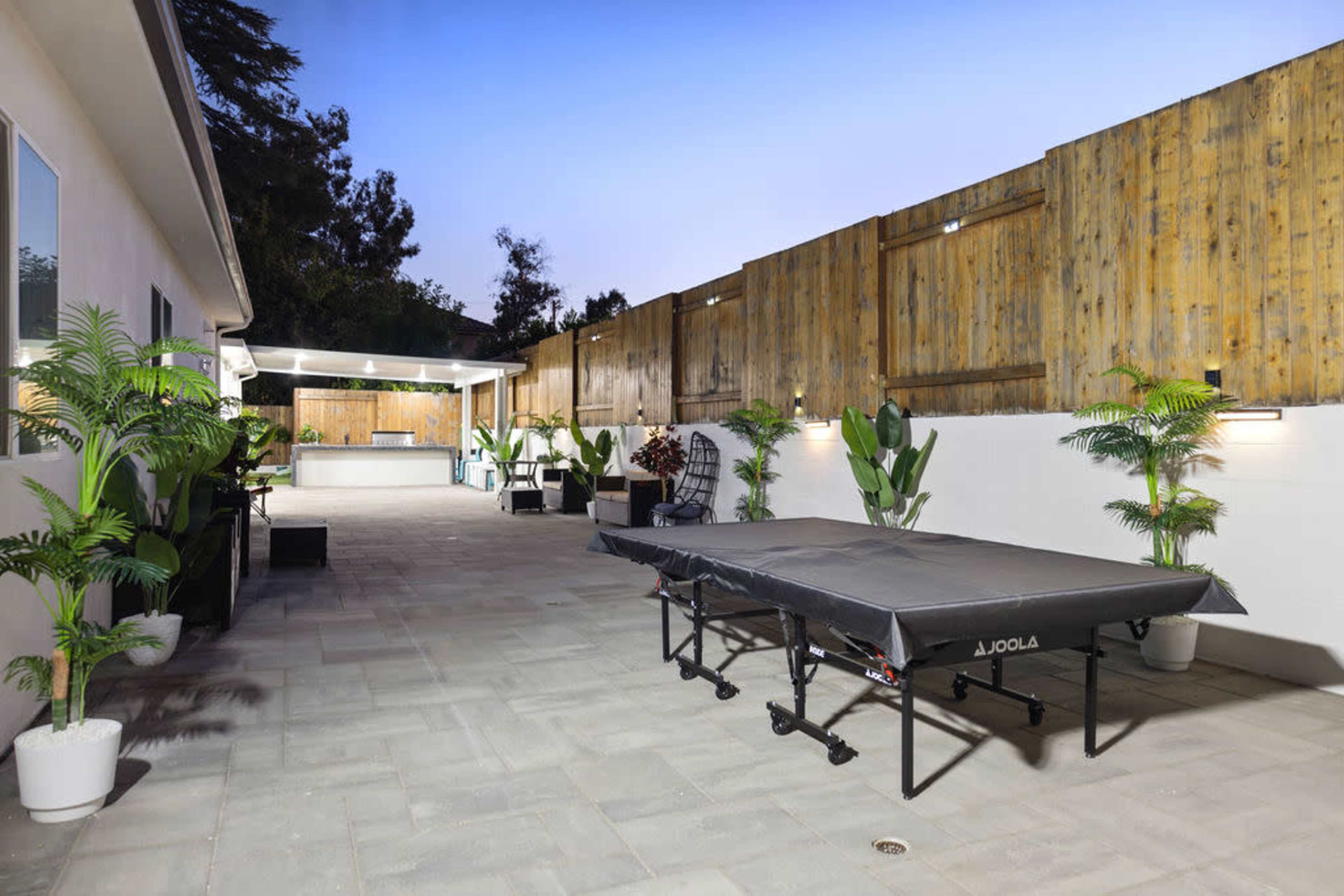 A spacious backyard with a ping pong table and well-maintained landscaping, featuring potted plants and a wooden fence.