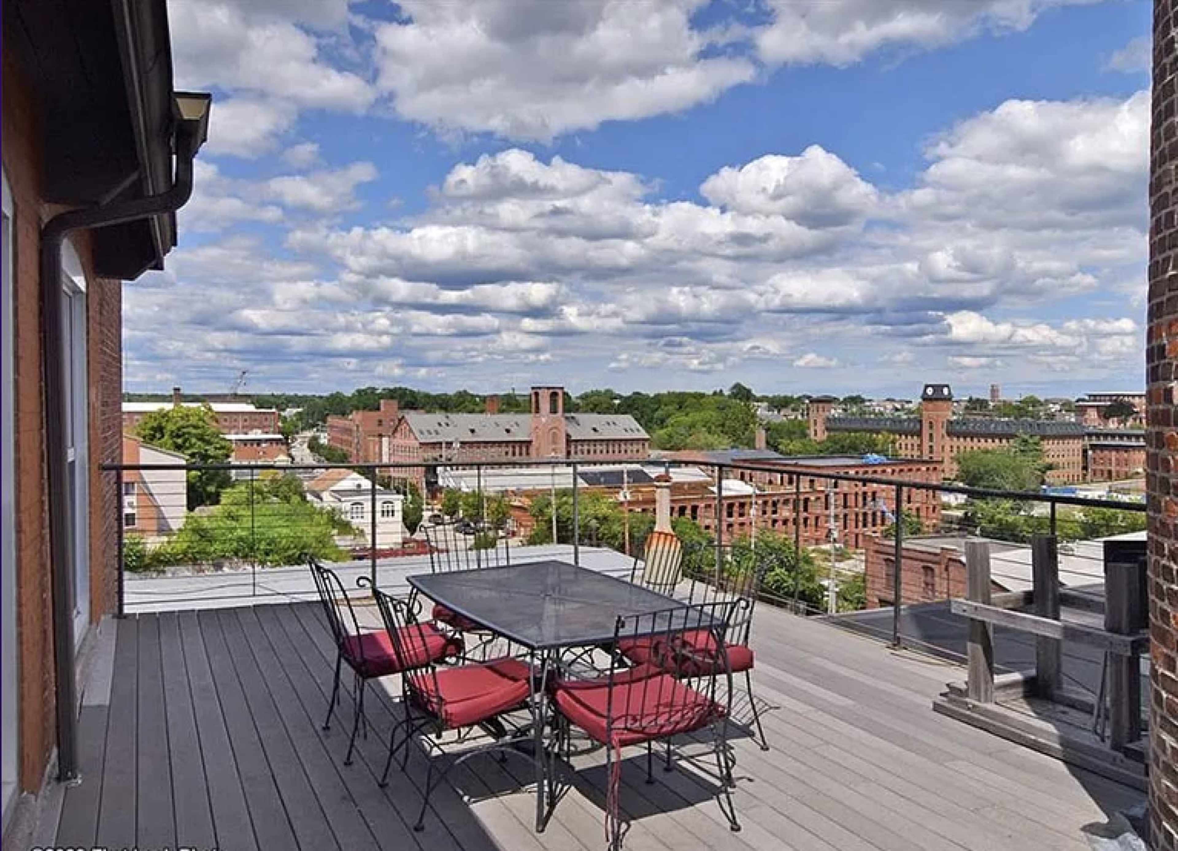 A rooftop patio with a metal dining table and chairs overlooking a cityscape under a cloudy sky.