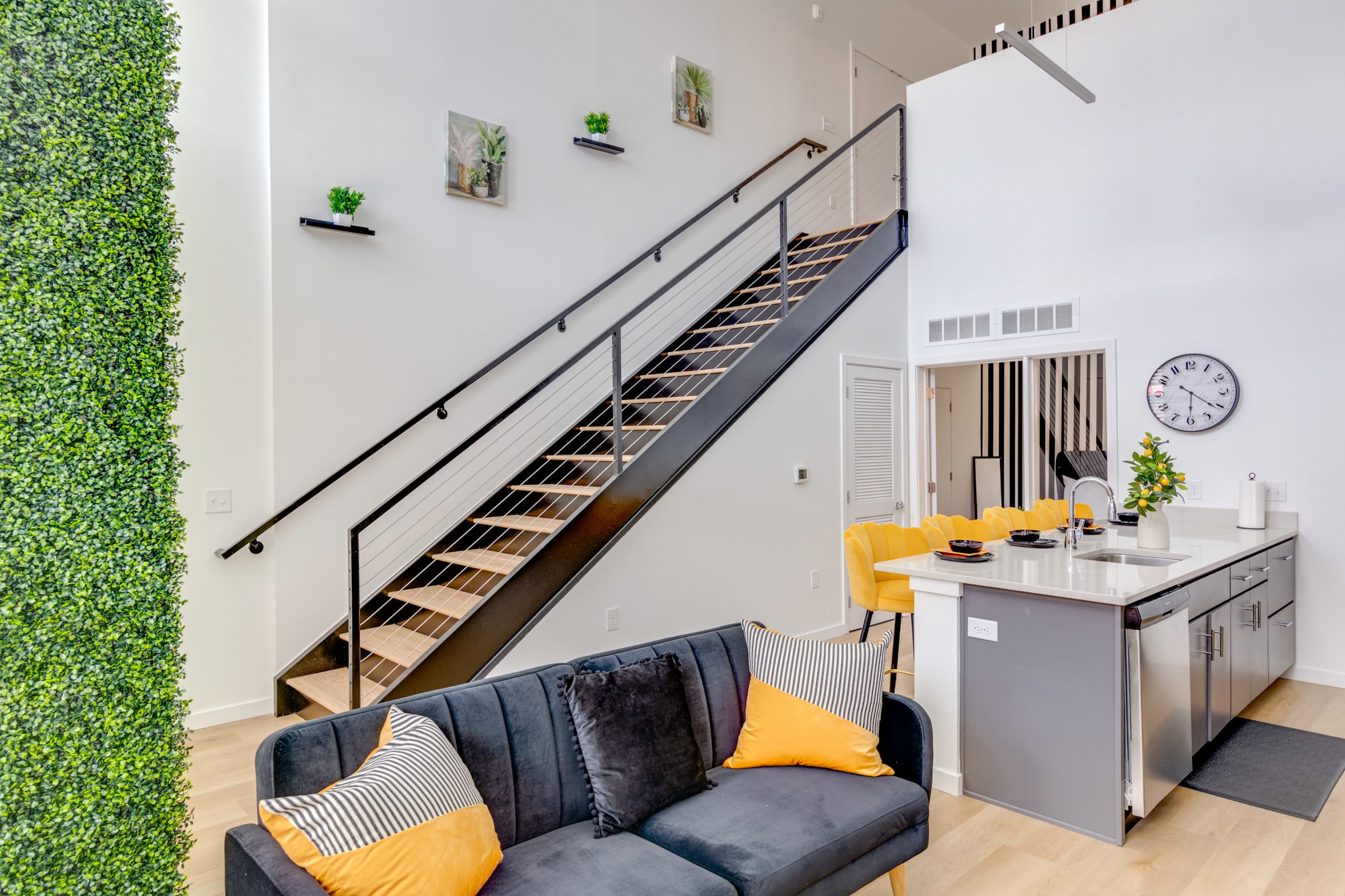 A modern, open-concept living space with a staircase, a kitchen island, and a sofa adorned with decorative pillows.