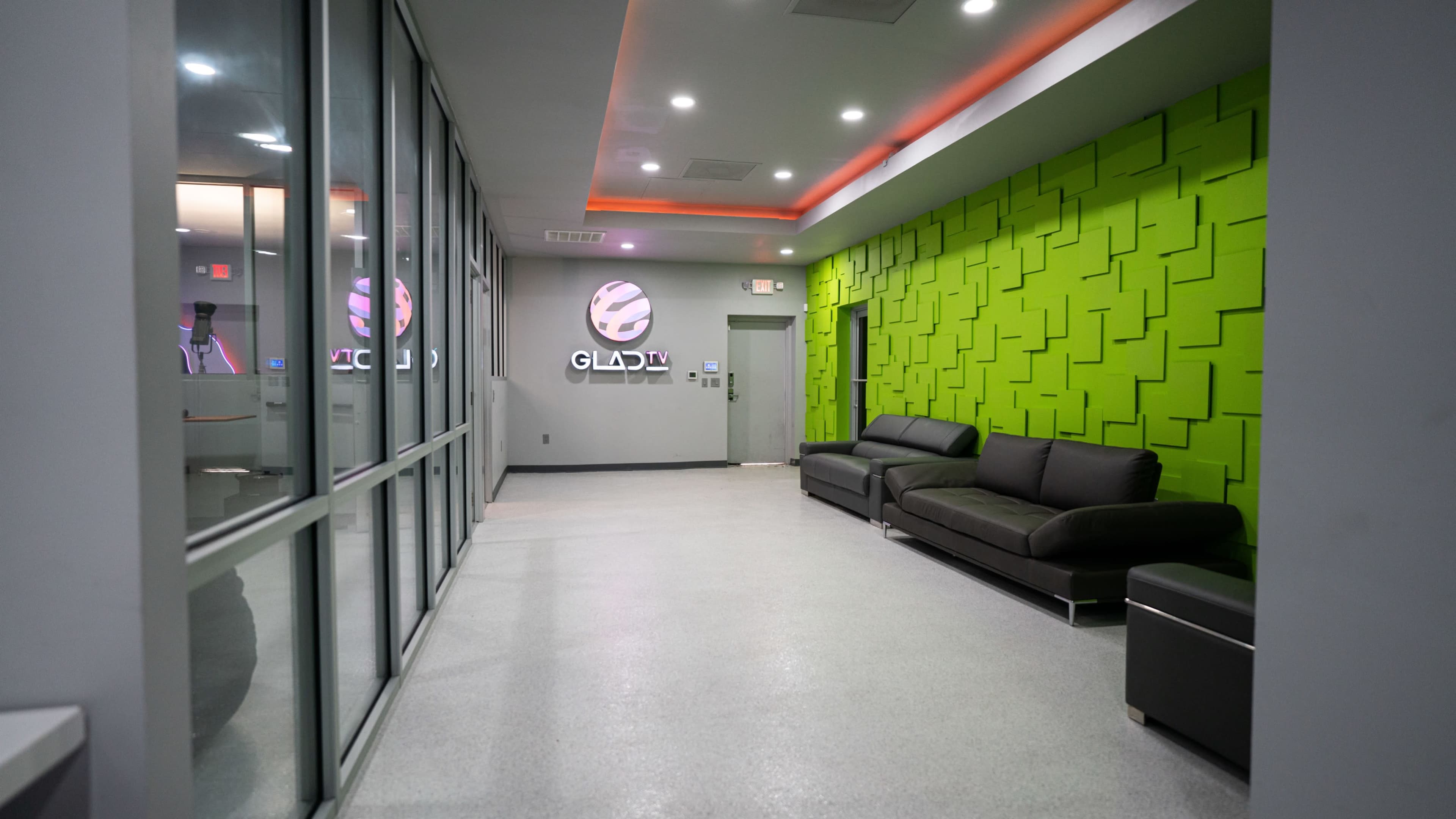 A modern hallway with a green textured wall, a black sofa, and large glass windows.
