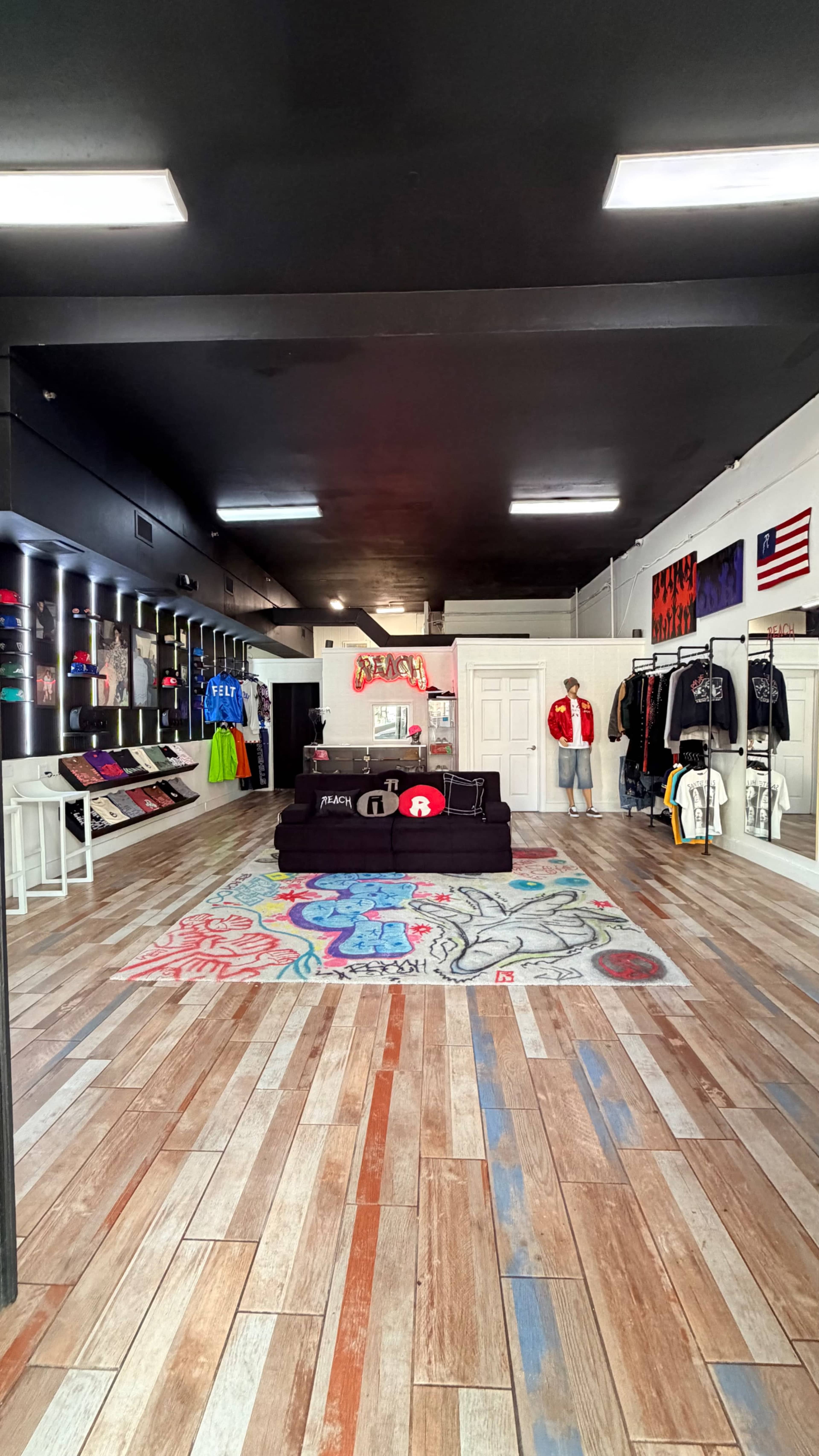 The image shows a clothing store interior featuring a colorful rug in the center, racks of apparel on the sides, and merchandise displayed on a black couch.