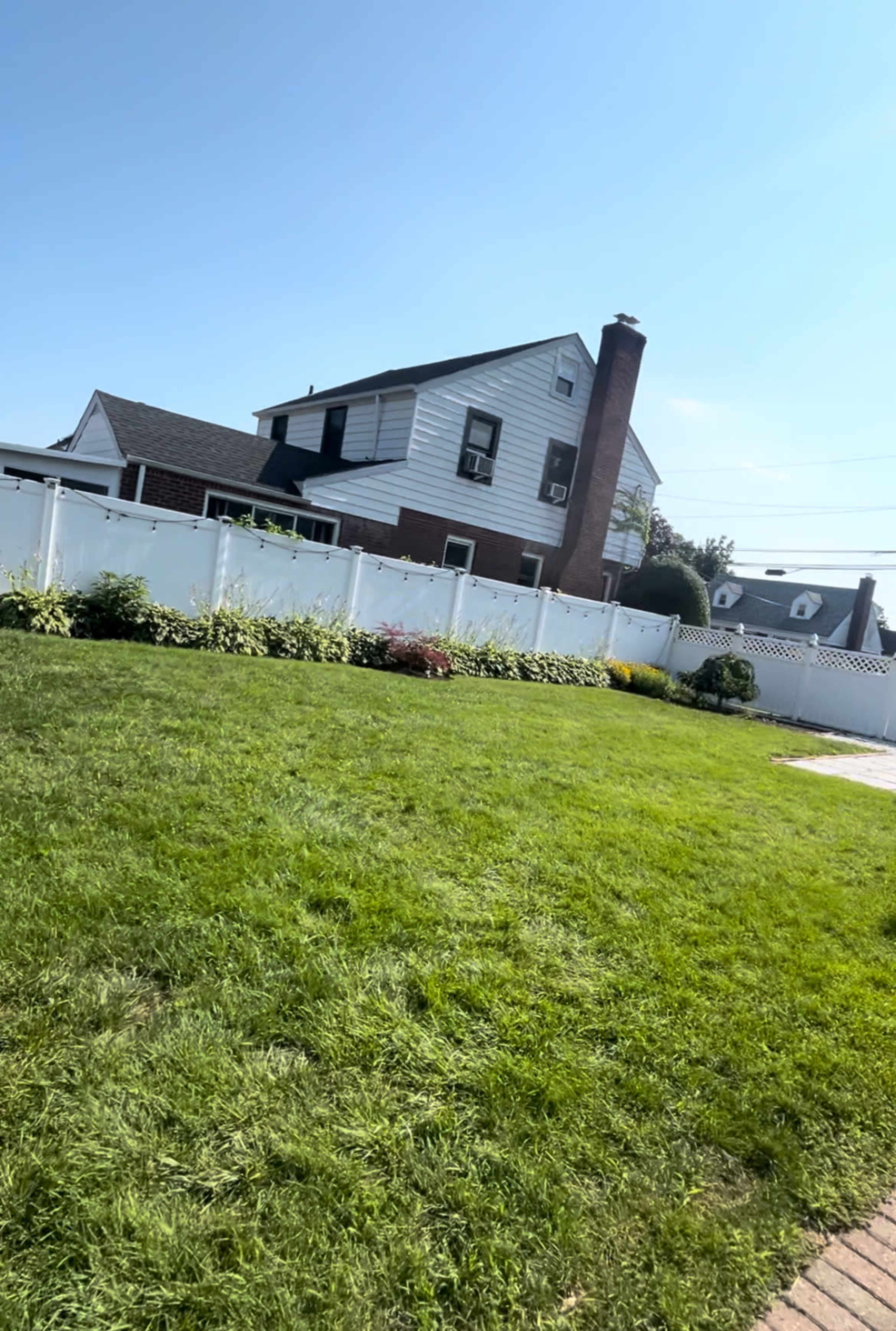 A house with a white fence and a well-maintained yard is shown under a clear blue sky.