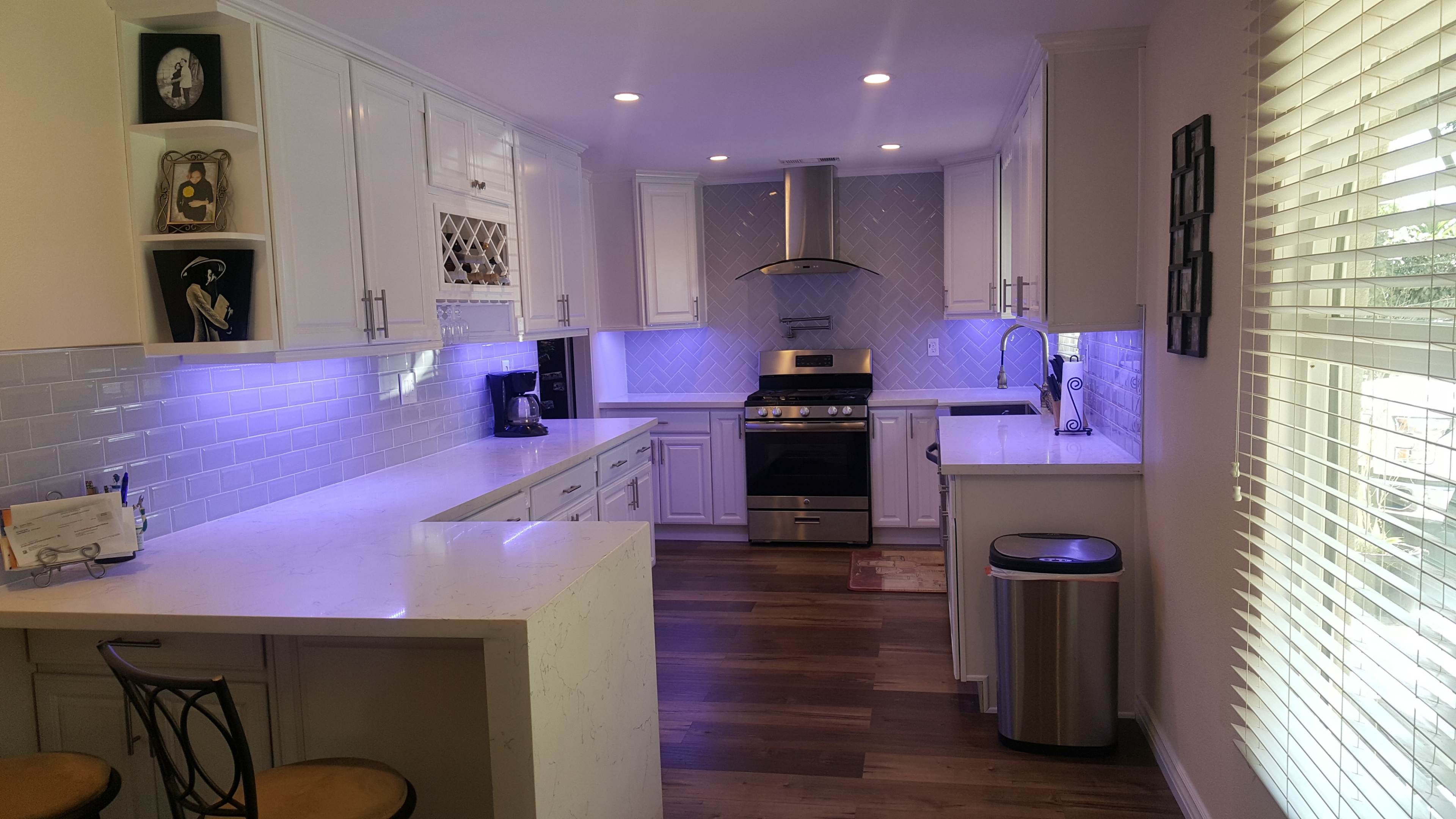 A modern, white kitchen featuring stainless steel appliances, a large island with stools, and bright lighting.