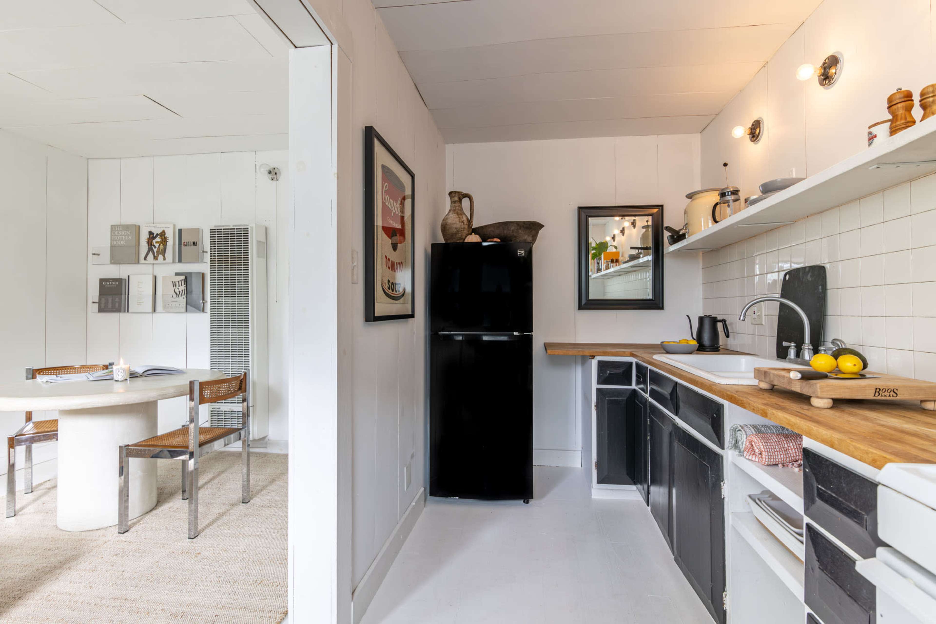 The image shows a compact kitchen area with black and white cabinetry, a small dining table, and modern appliances.