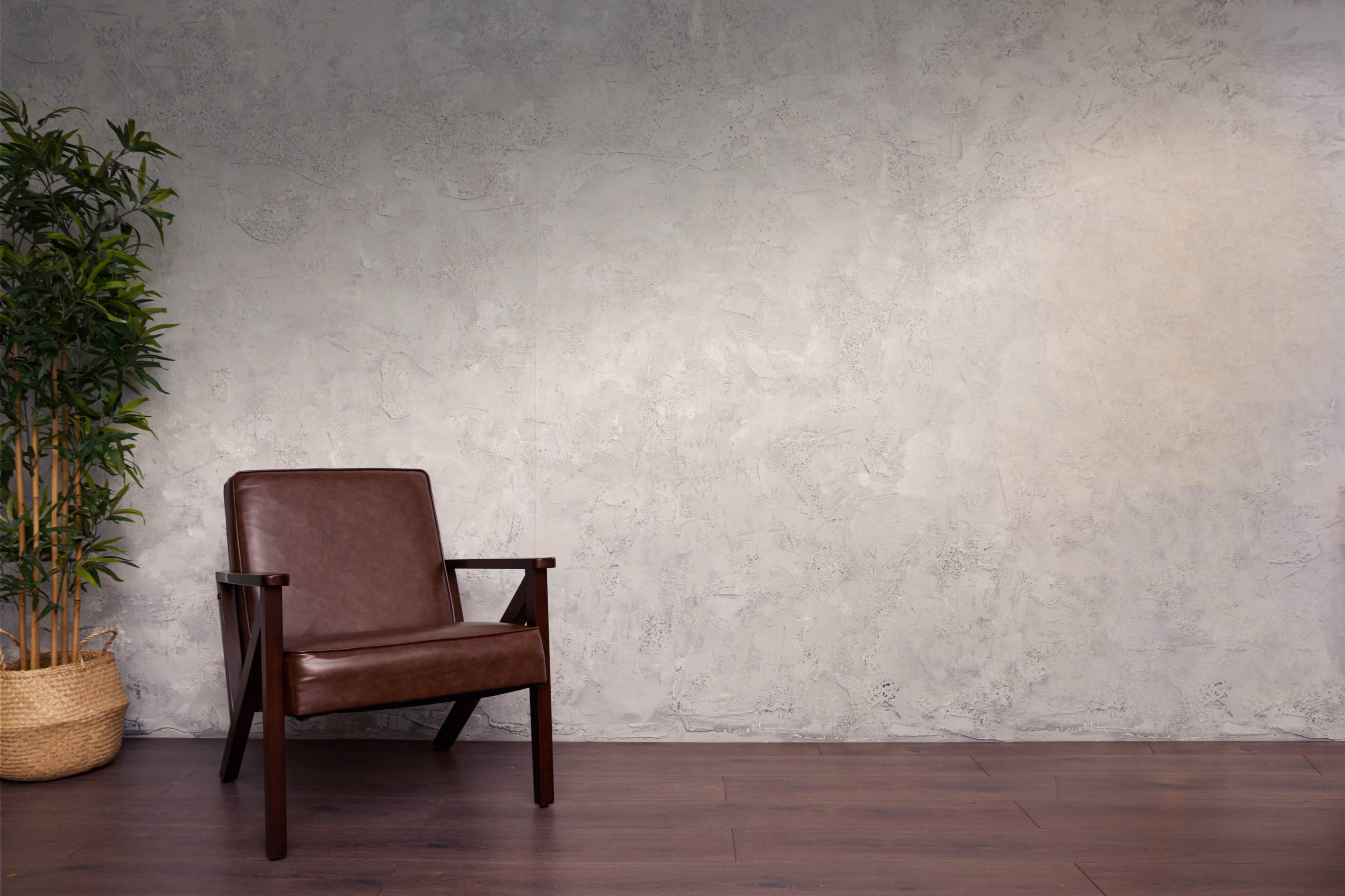 A brown leather chair is positioned against a textured gray wall with bamboo in a woven basket nearby.