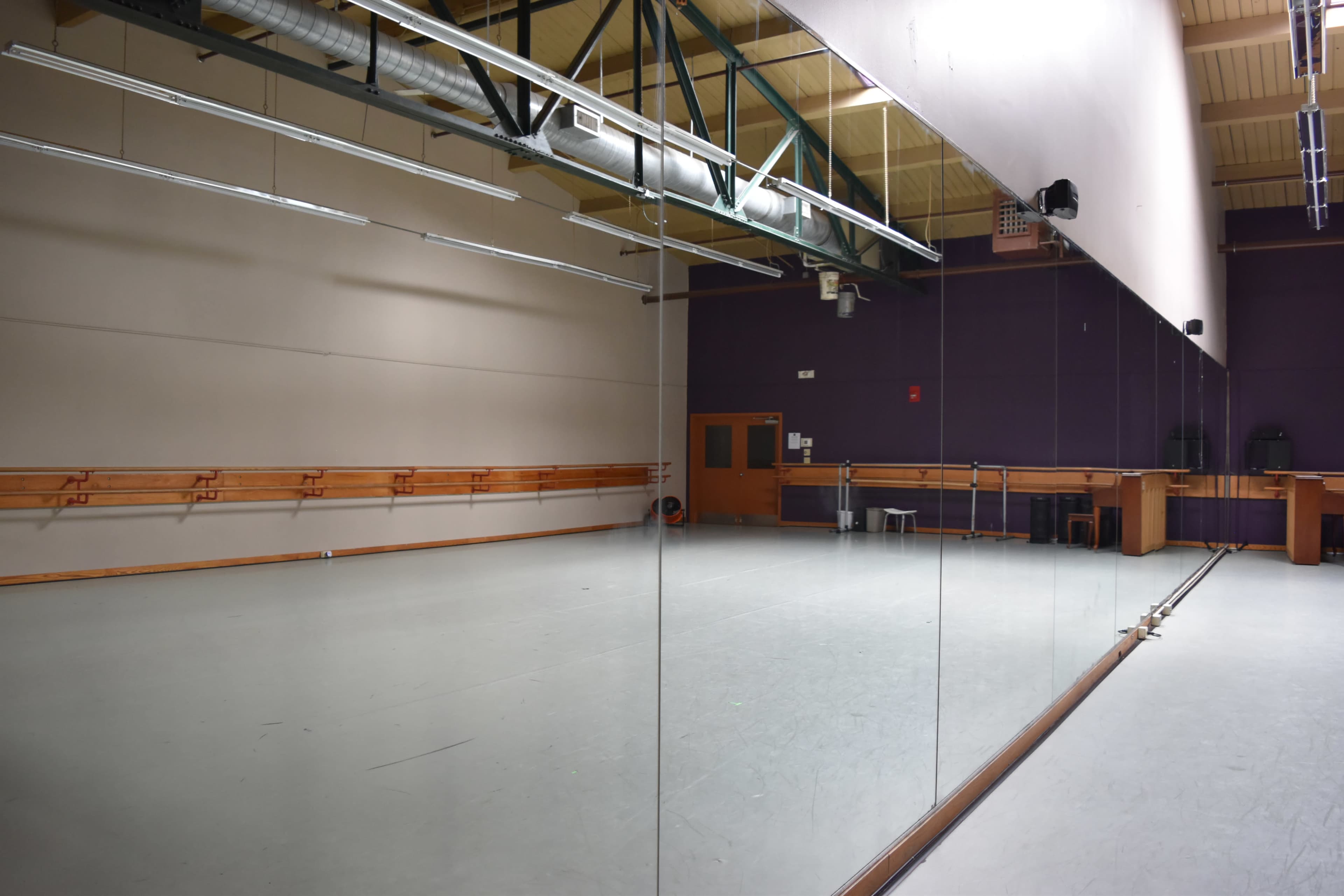 The image shows a spacious dance studio with wooden ballet bars, a large mirror, and a glossy floor.