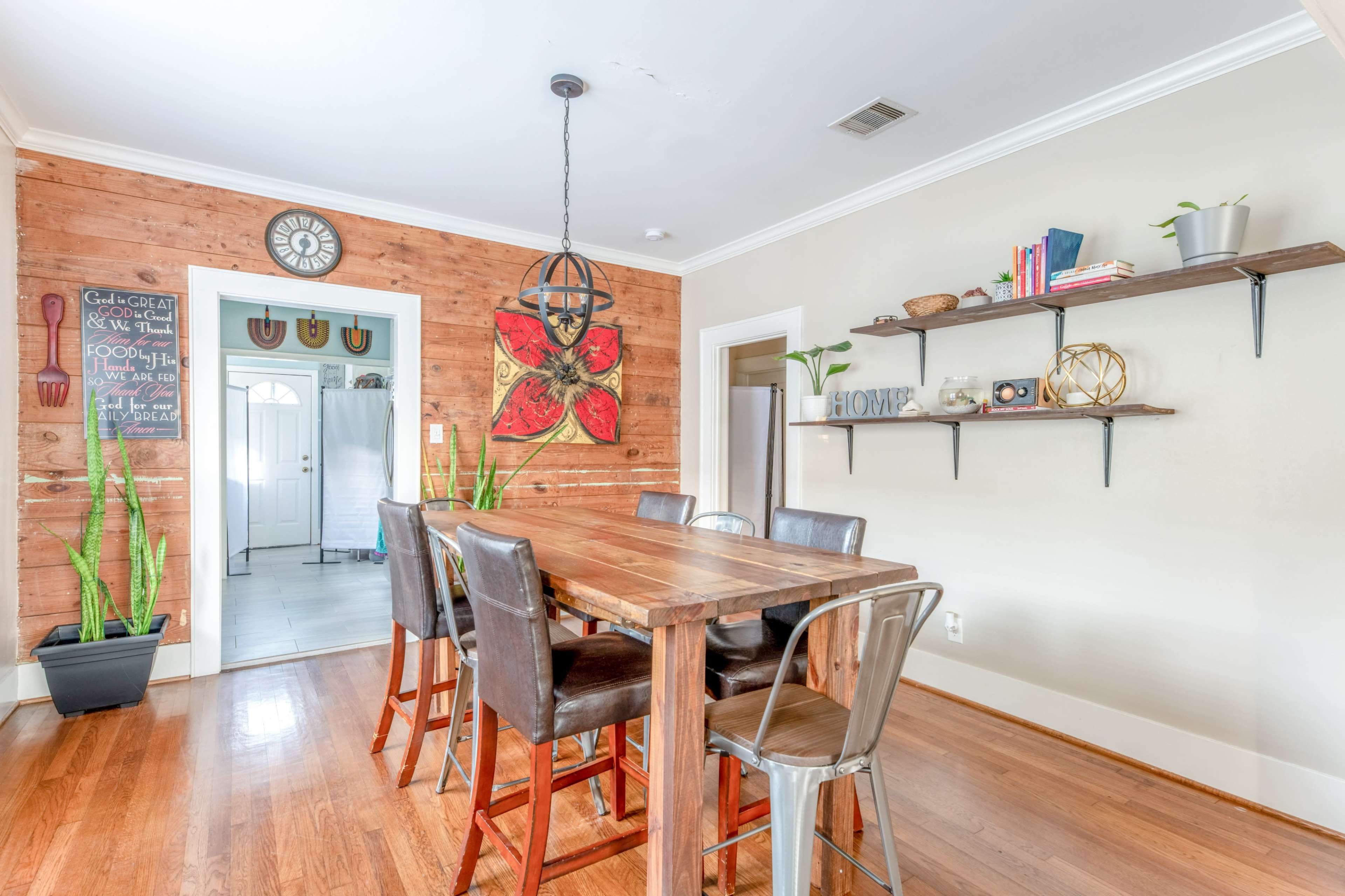 A dining area features a wooden table surrounded by metal chairs, with a wall adorned by shelves and decorative items.