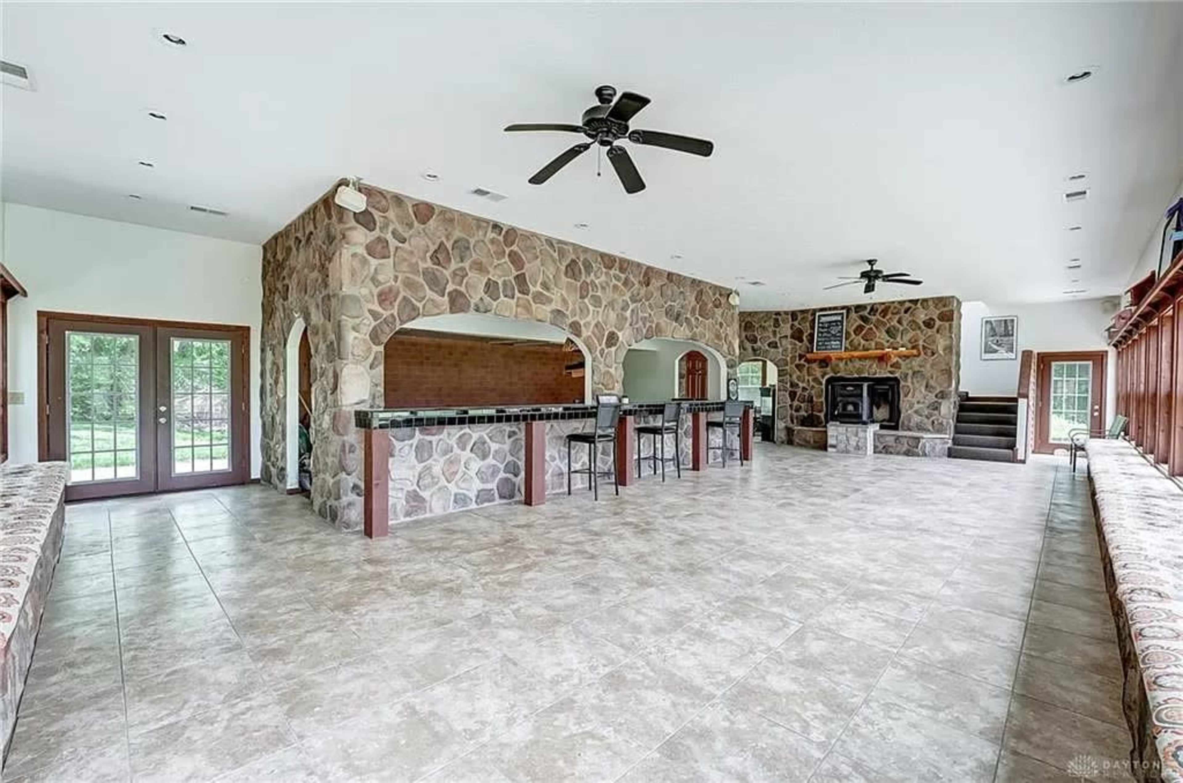 A spacious room with stone walls, a bar area, and large windows overlooking a green outdoor scene.