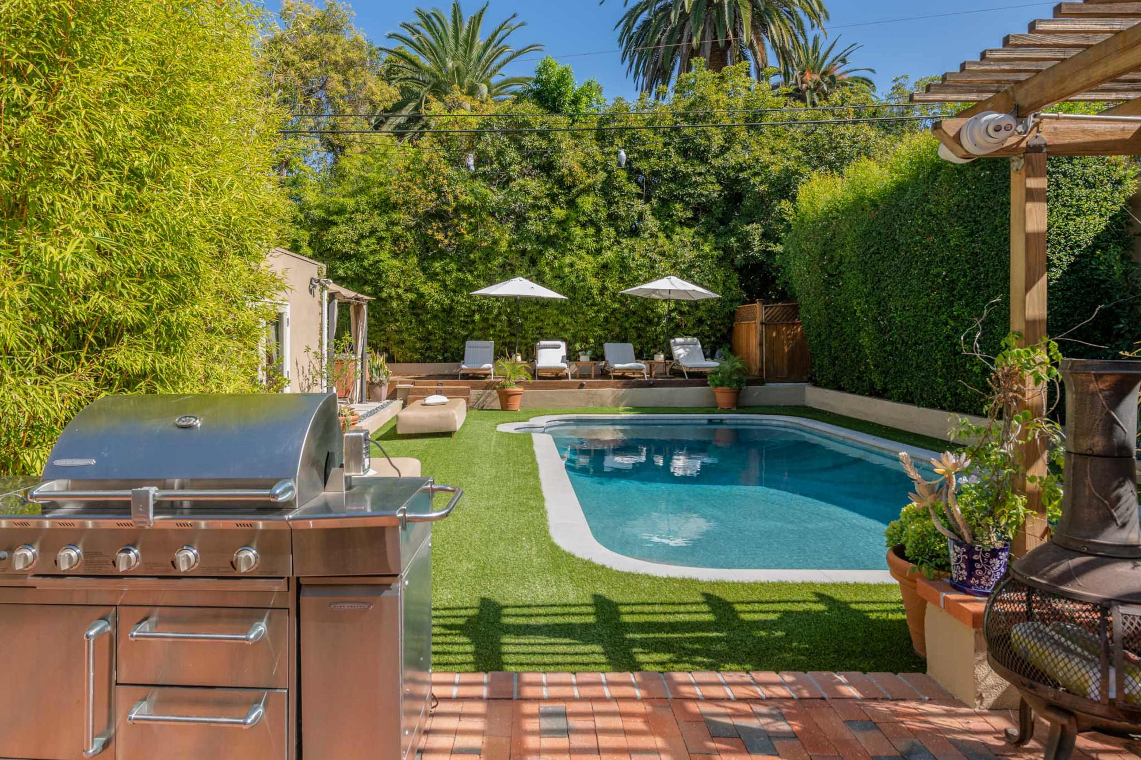 The image shows a backyard pool area with a barbecue grill, lounge chairs, and lush greenery surrounding the pool.