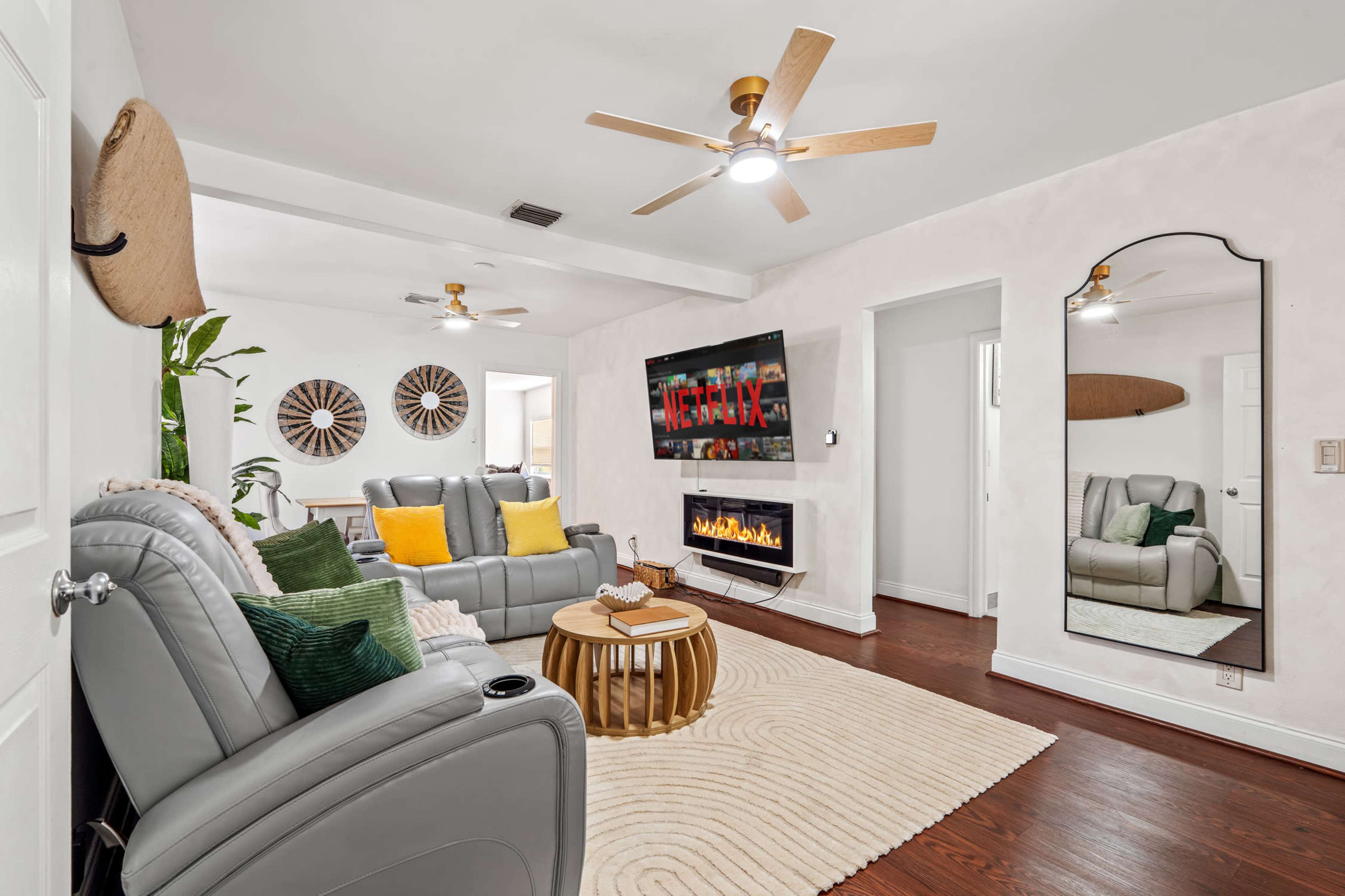The living room features gray leather seating, a large television mounted on the wall, a circular wooden coffee table, and a decorative area rug.