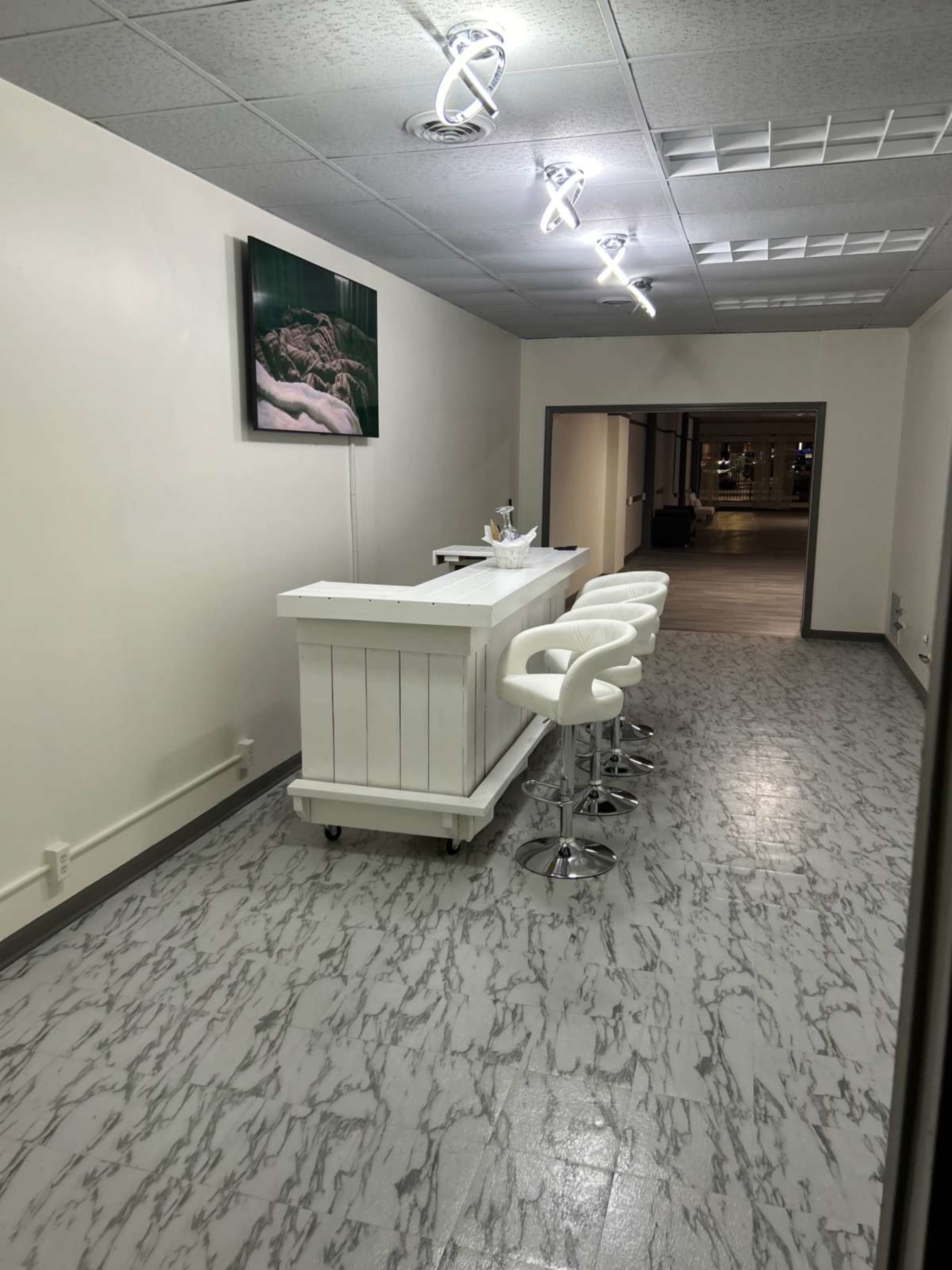 The image shows a modern, minimalist interior with a white bar counter and four high stools on a marbled floor.