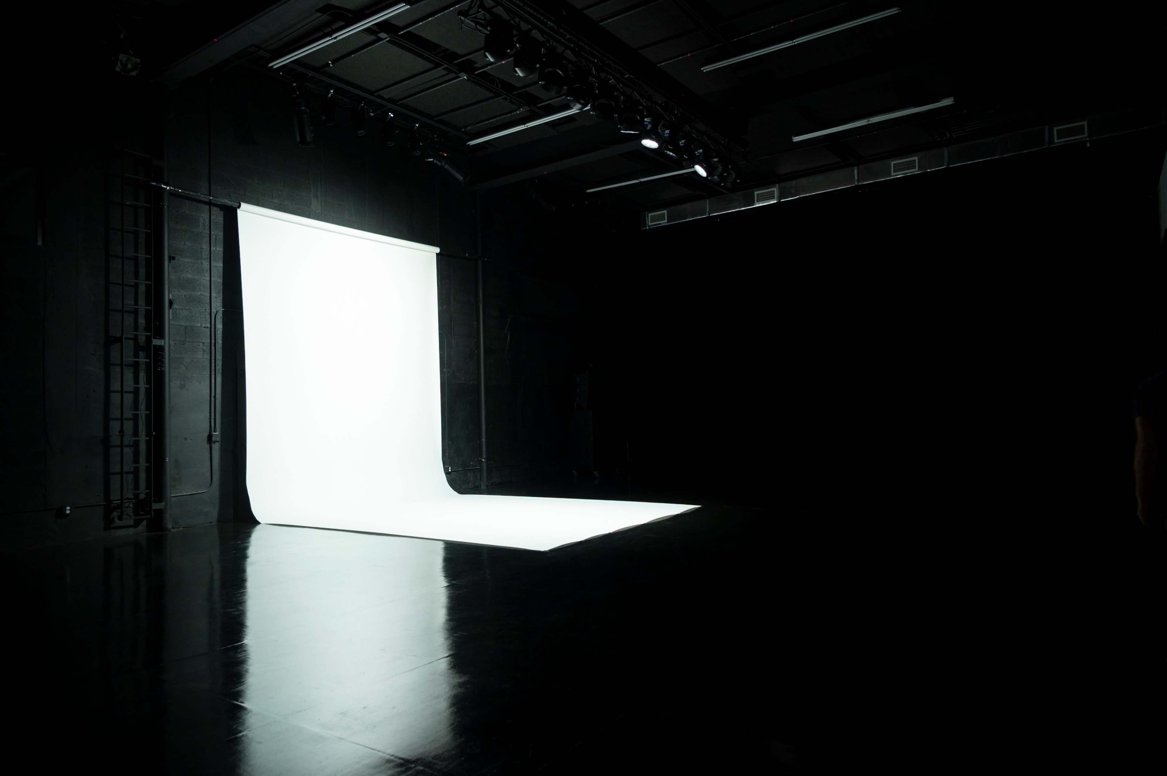 A brightly lit, white backdrop is positioned in an otherwise dark studio space.