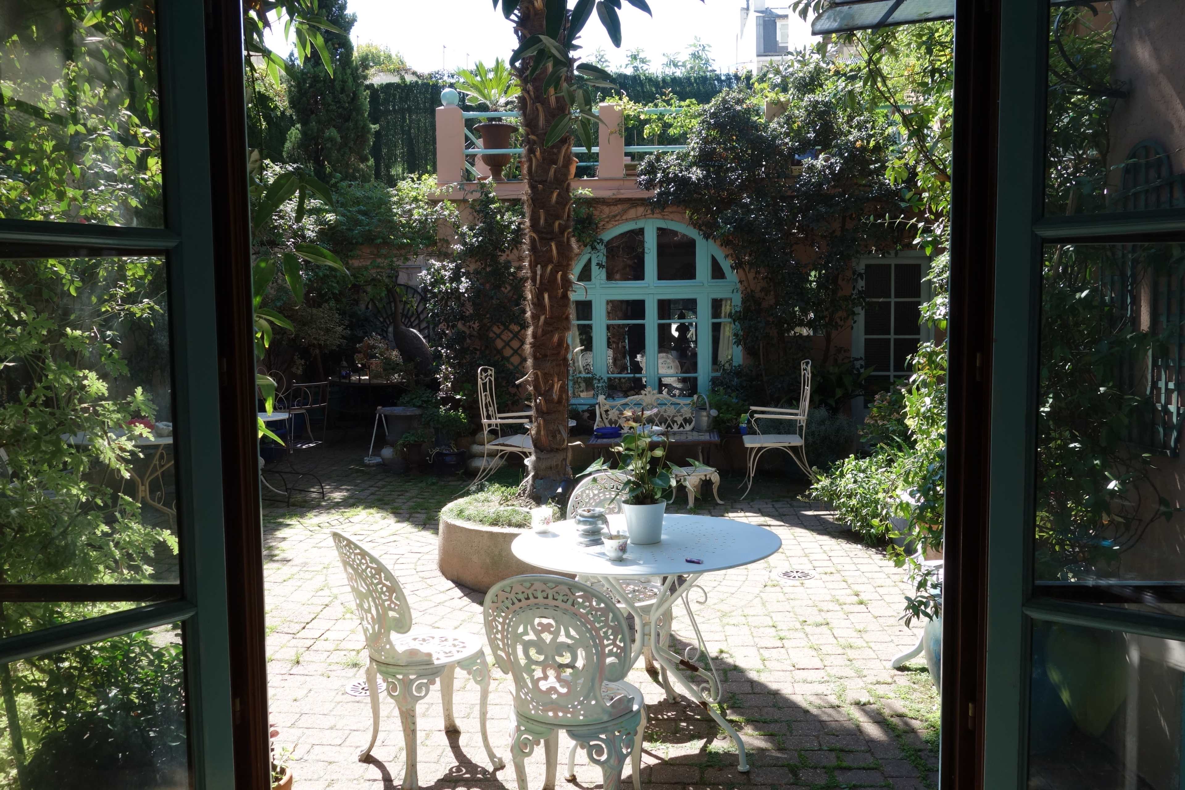 A well-maintained courtyard features a round table and chairs surrounded by greenery and various plants.