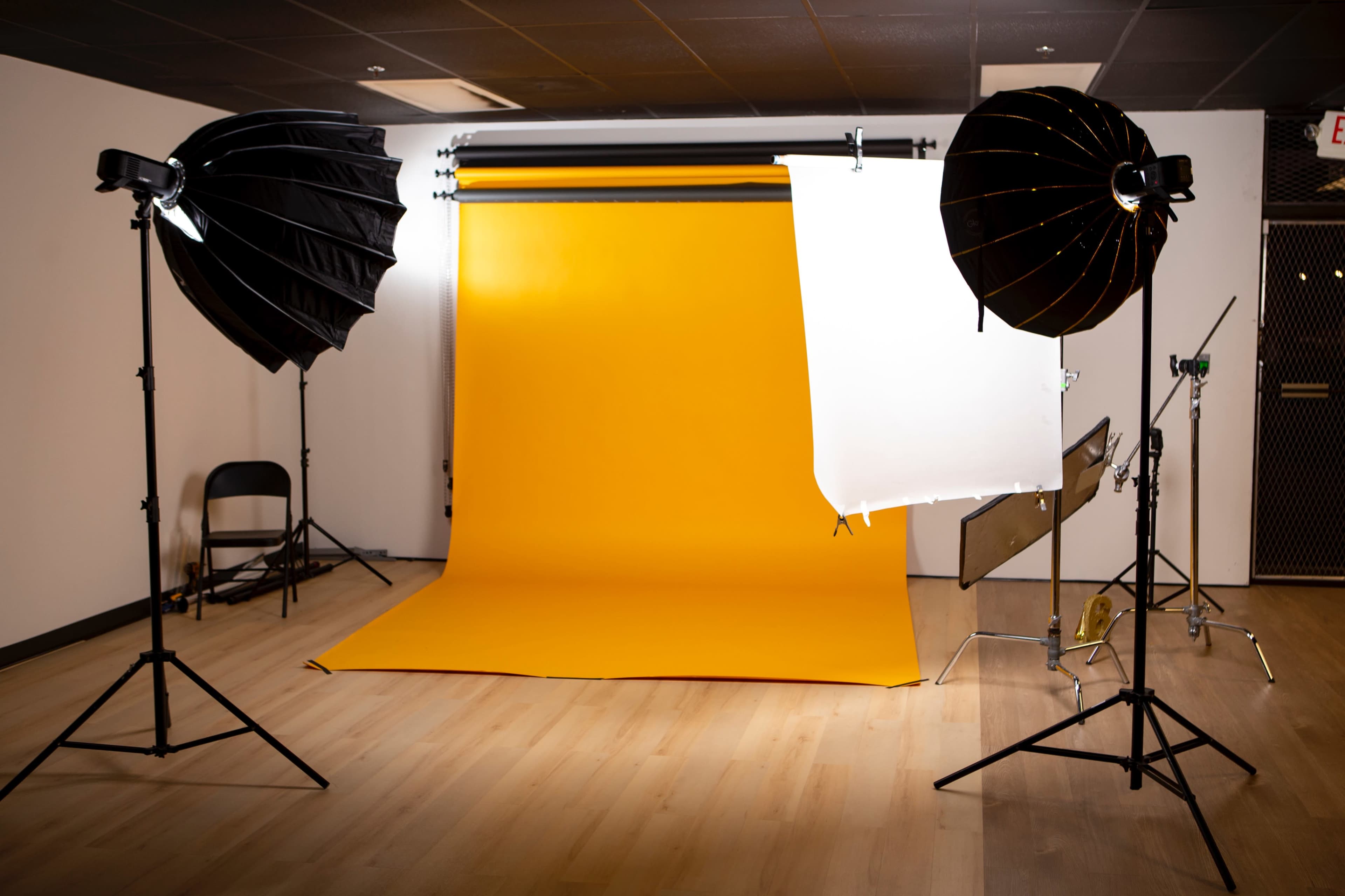 A photography studio with a yellow backdrop, two light setups, and a foldable chair.