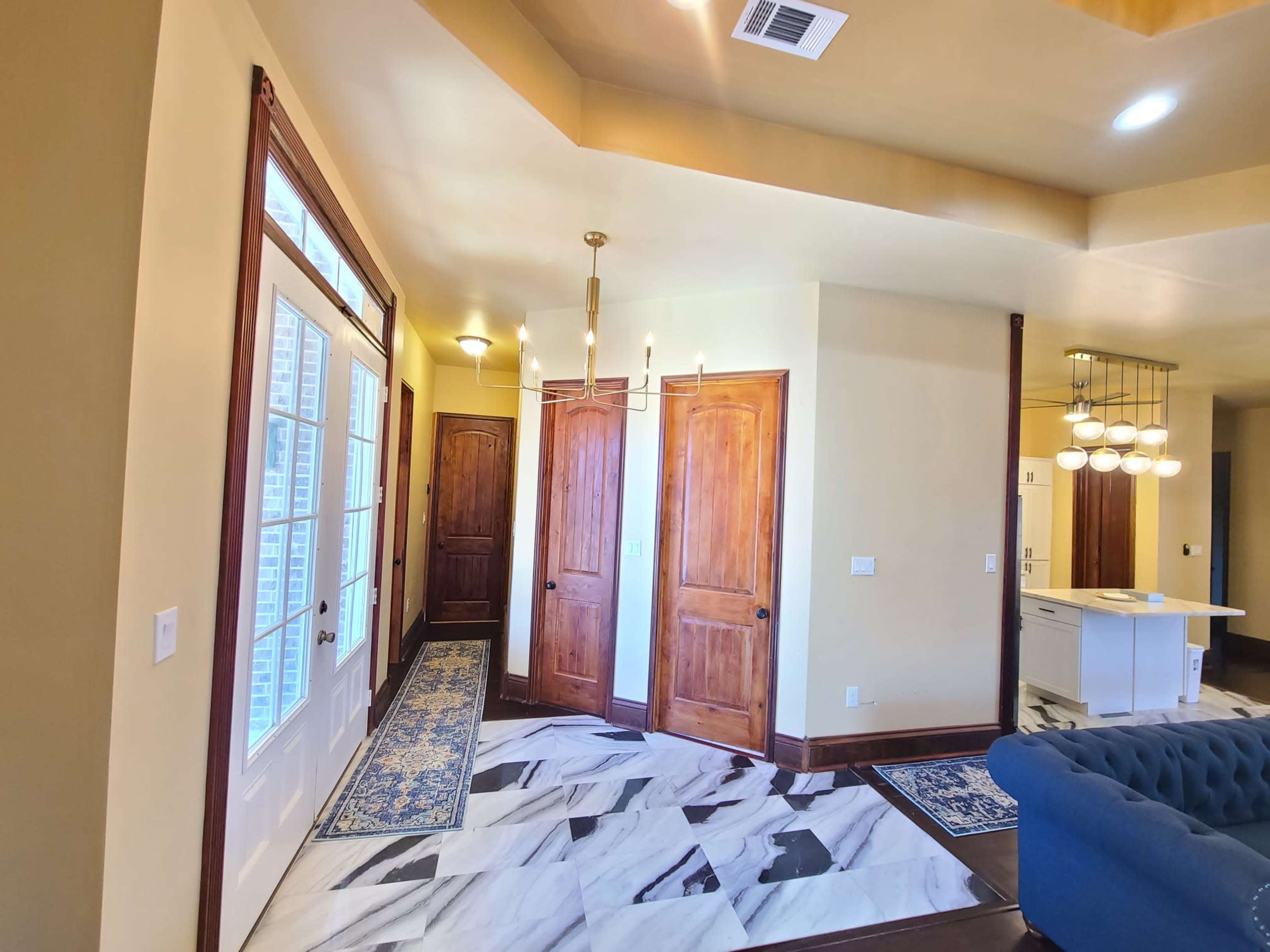 A foyer with marble flooring, wooden doors, and a view of adjacent rooms.