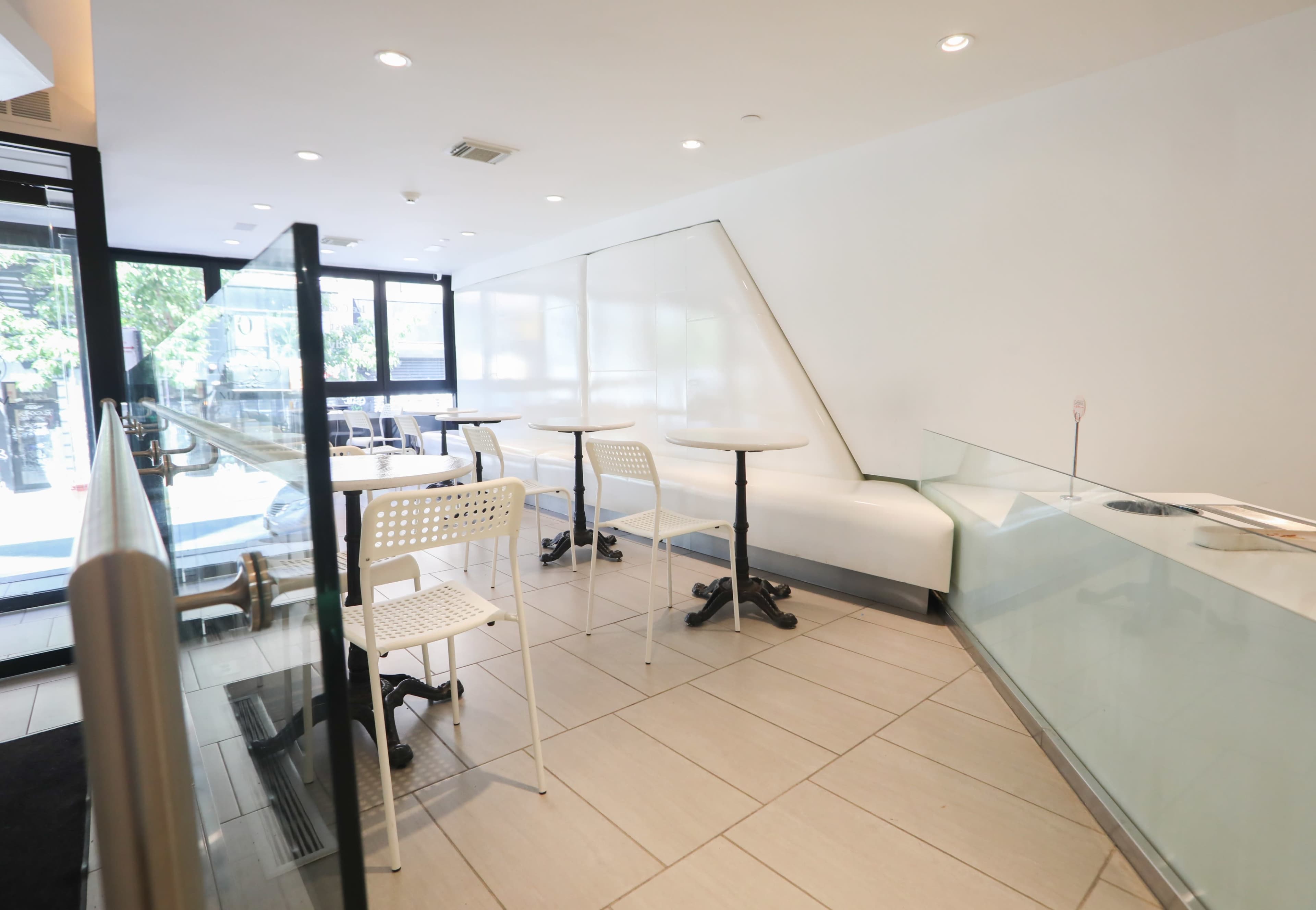 A modern, minimalist café interior with white walls, small round tables, and clear glass features.