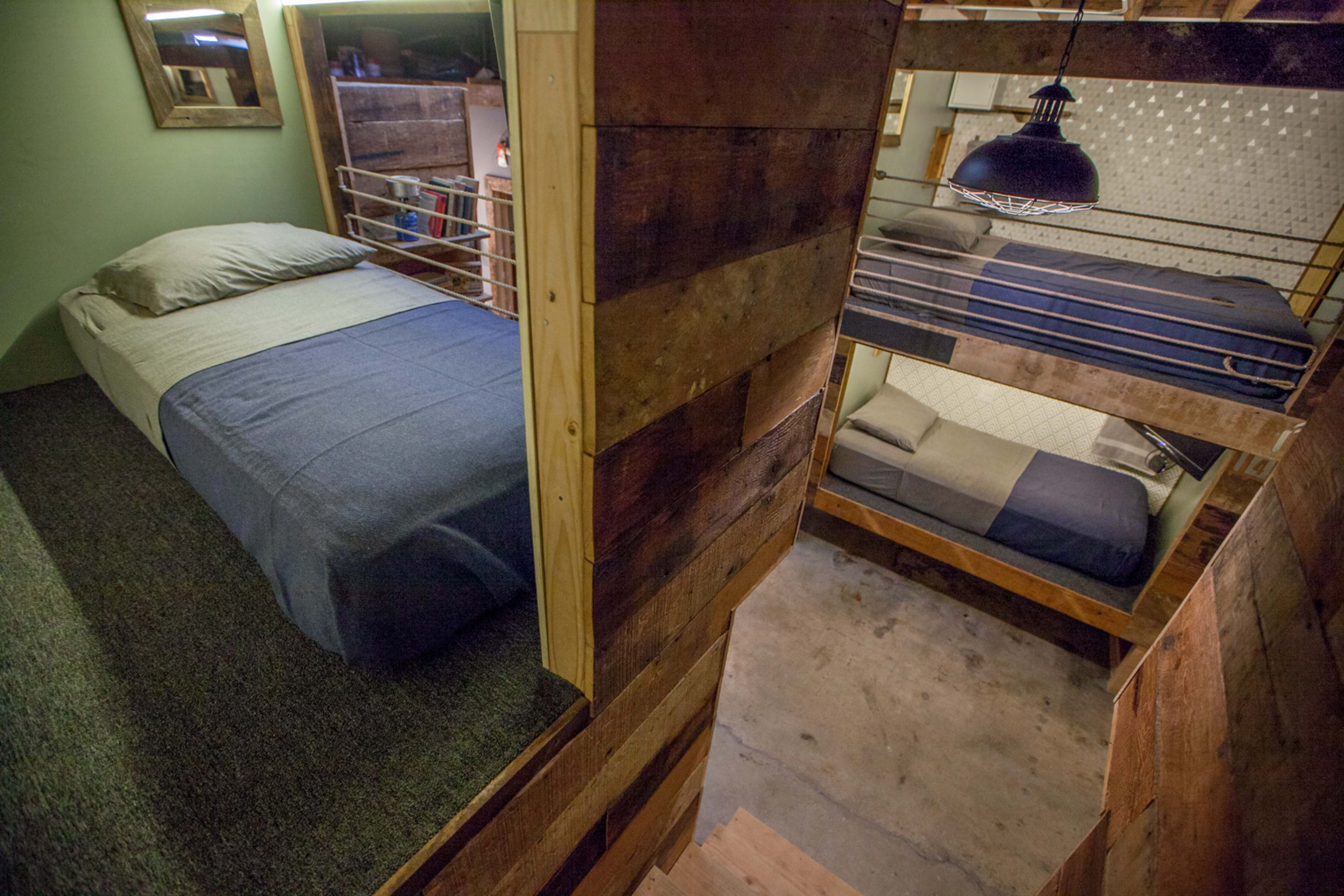 The image shows a multi-level sleeping area with wooden walls, featuring two beds, one above the other, separated by a staircase.