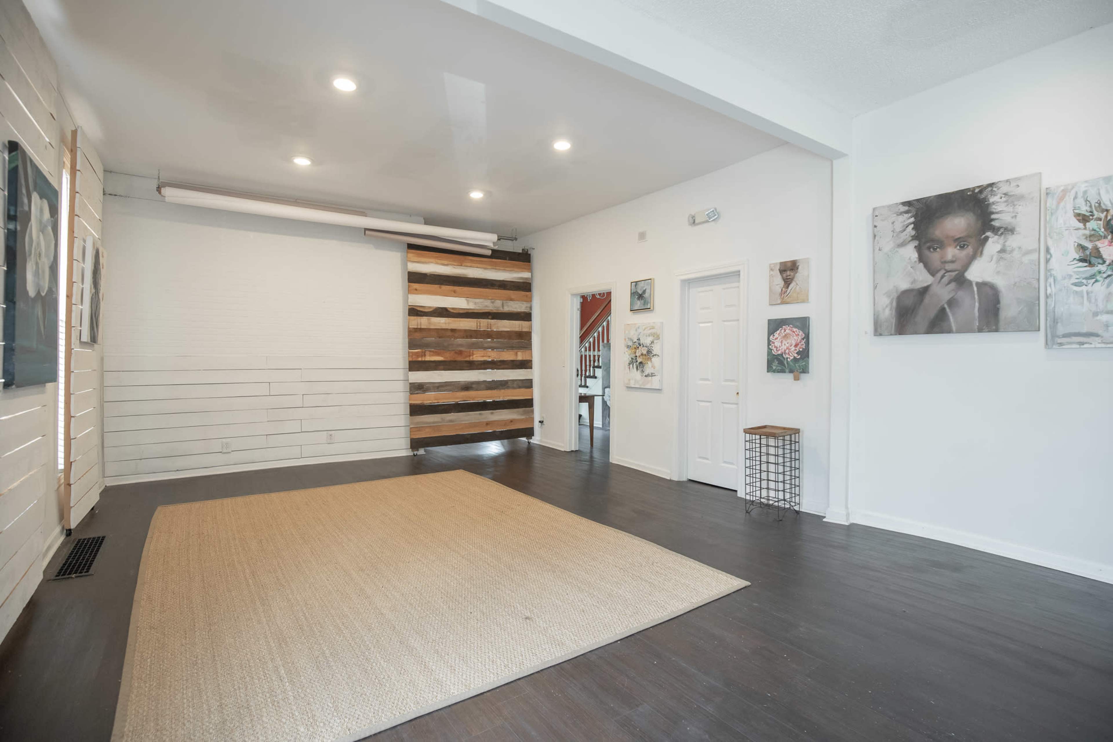 The room features a wooden floor, white walls, and a wall with a rustic wooden panel design, illuminated by overhead lights.