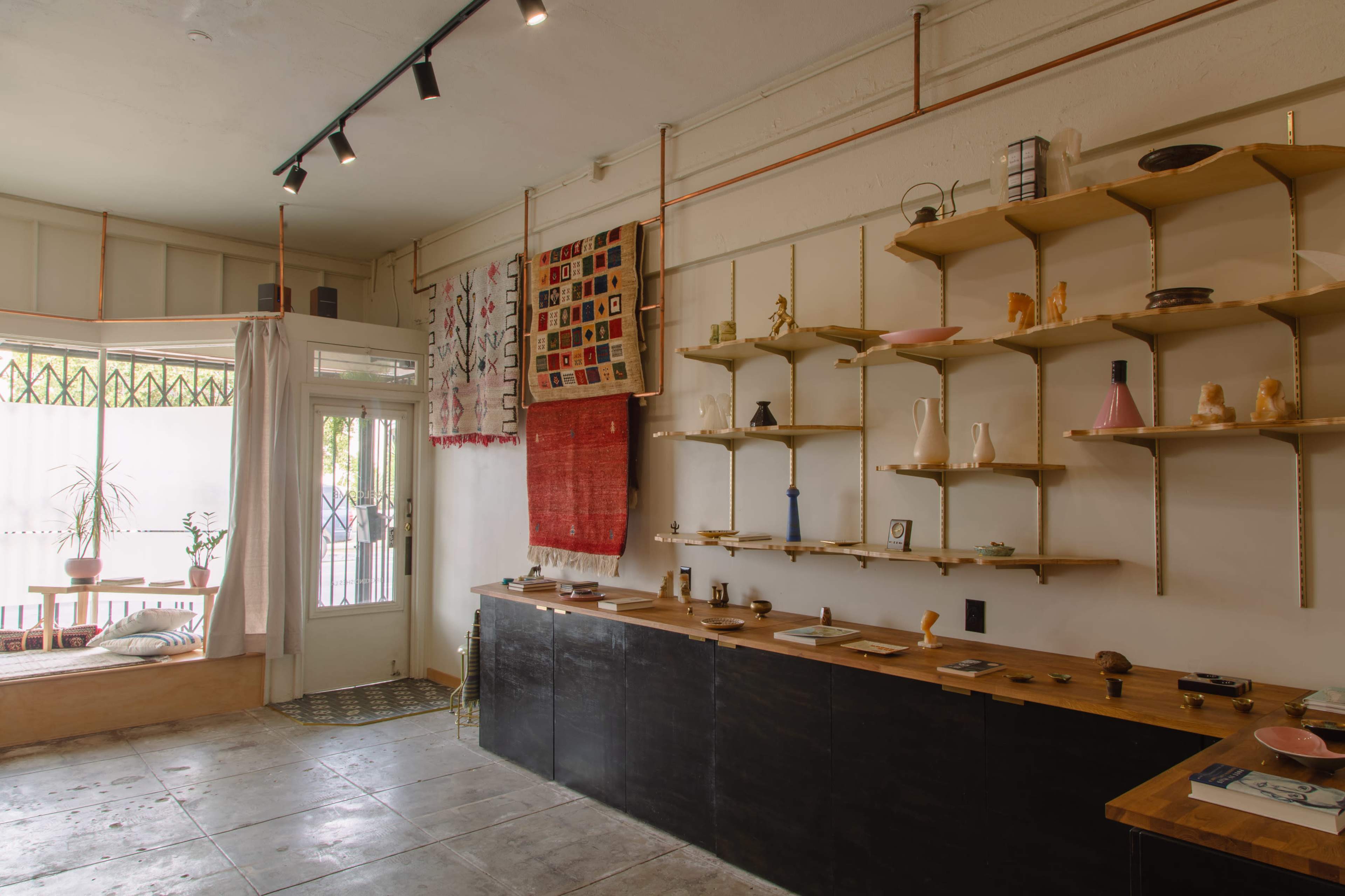 A minimalist retail space with wooden shelves displaying various decorative items and a large window allowing natural light inside.