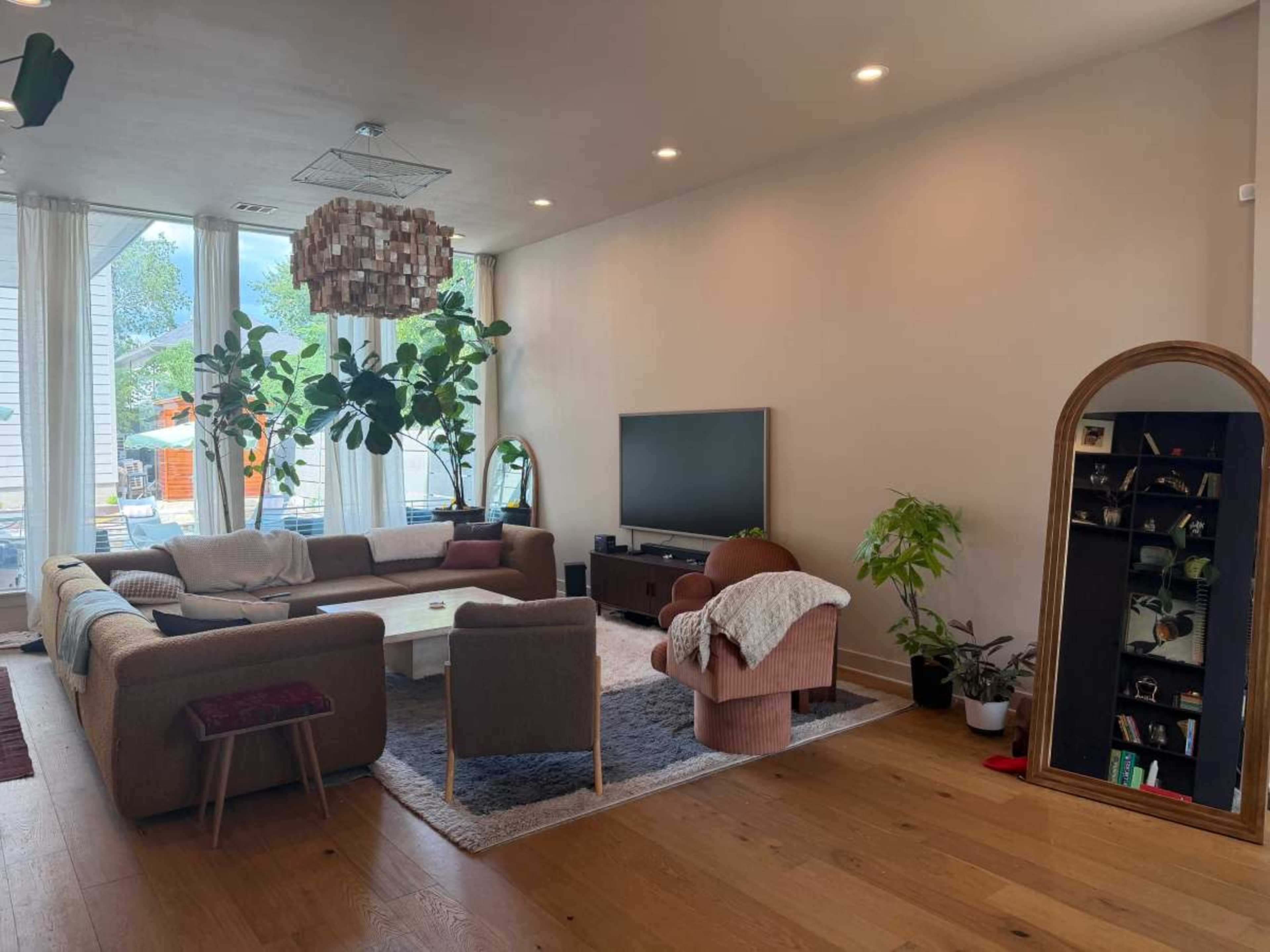 The image shows a spacious living room featuring a large sectional sofa, a coffee table, a television, and large windows allowing natural light to enter.