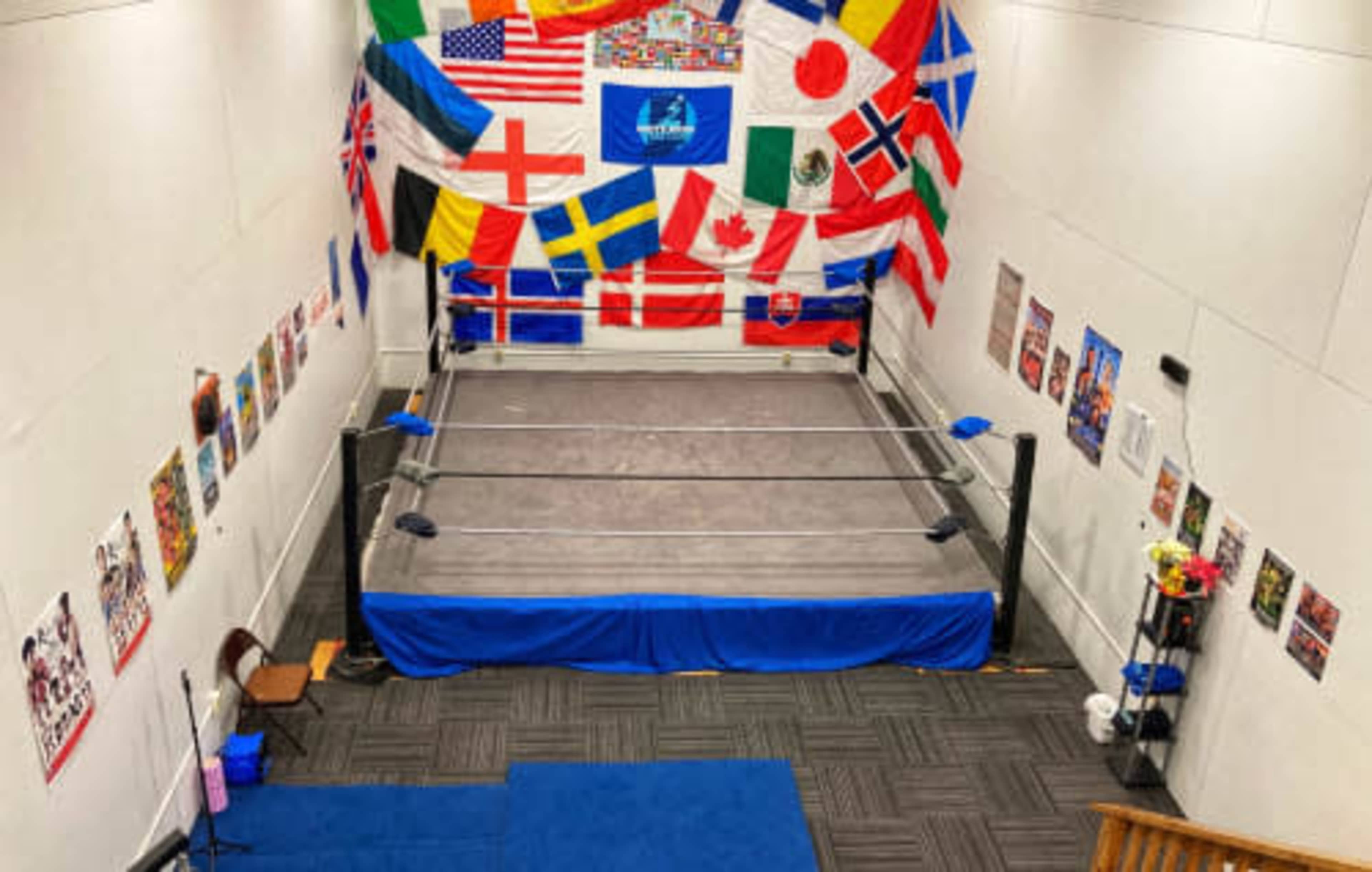 A wrestling ring surrounded by various national flags hanging on the wall and posters displayed nearby.