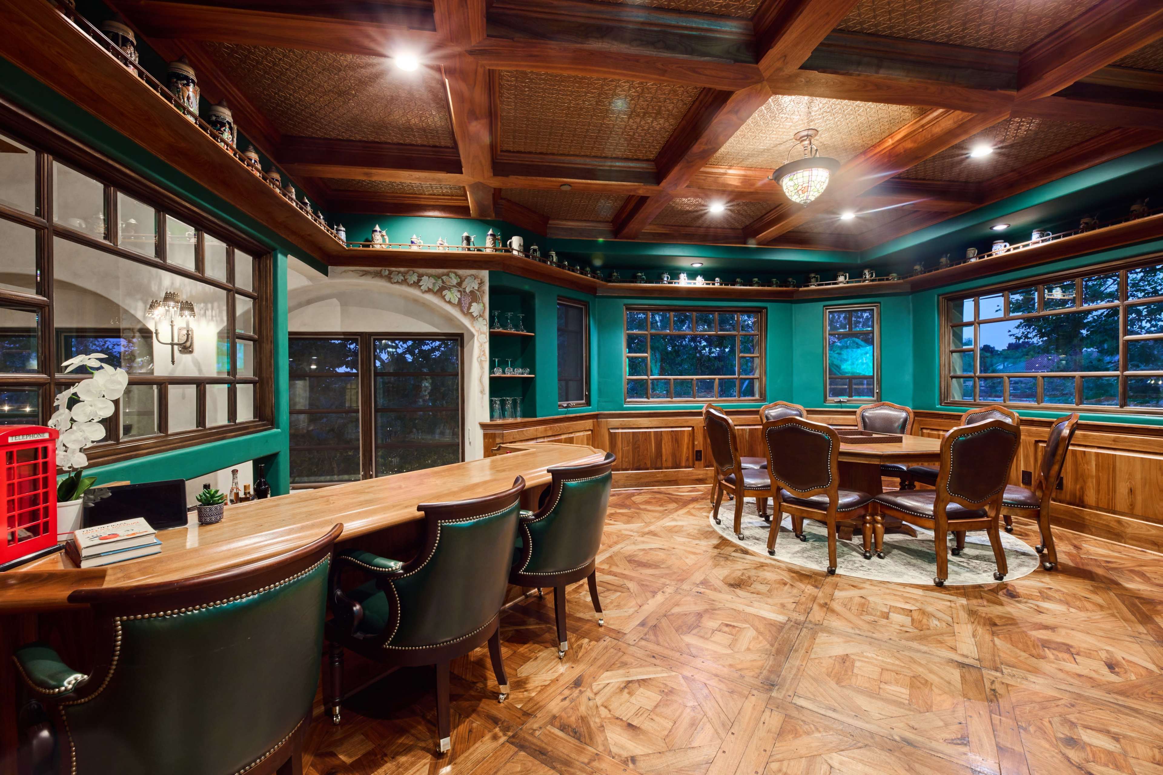 A well-decorated room with a wooden bar and seating area, featuring green walls and large windows.
