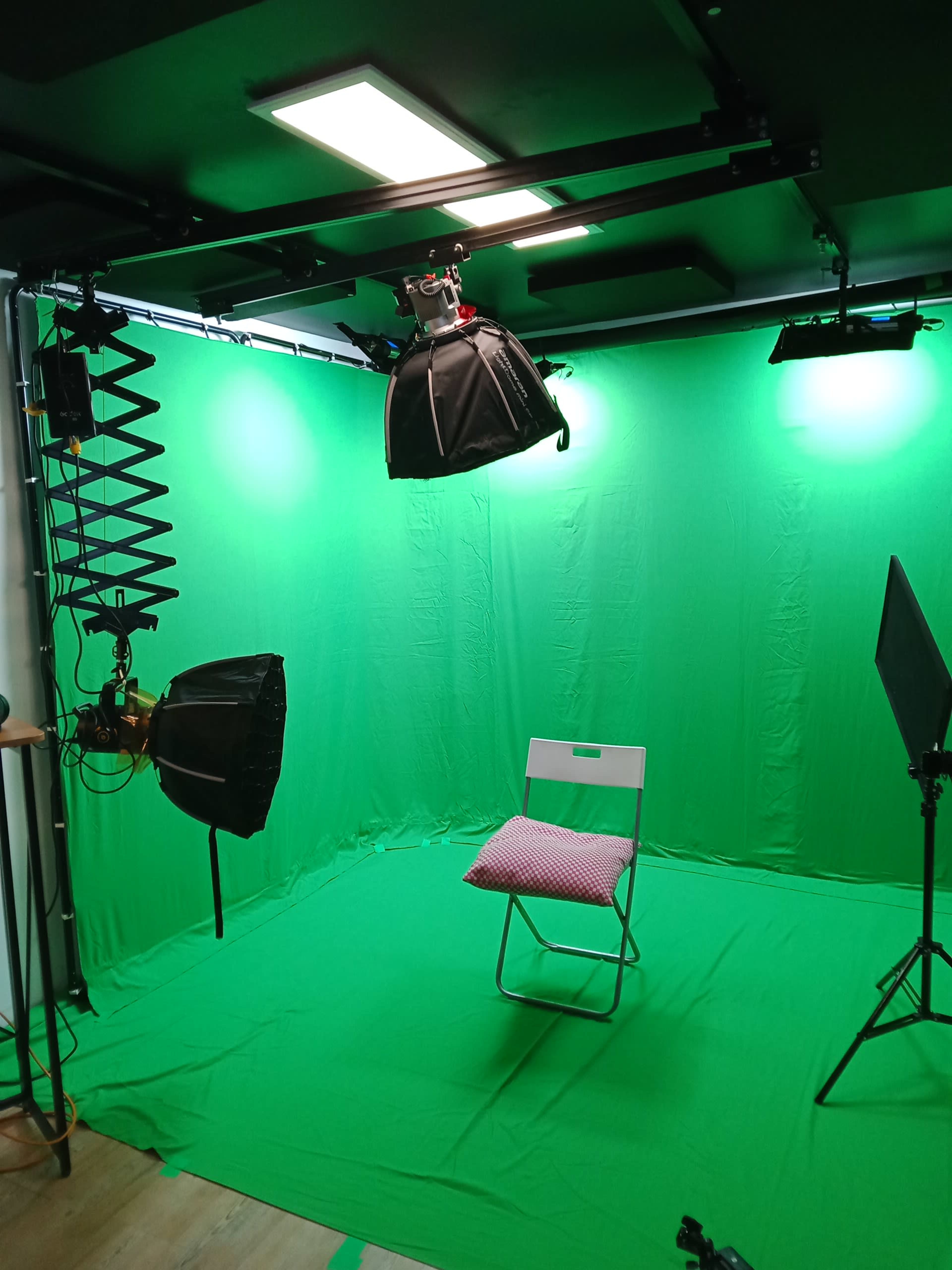 The image shows a green screen studio setup with a folding chair in the center, surrounded by various lighting equipment.