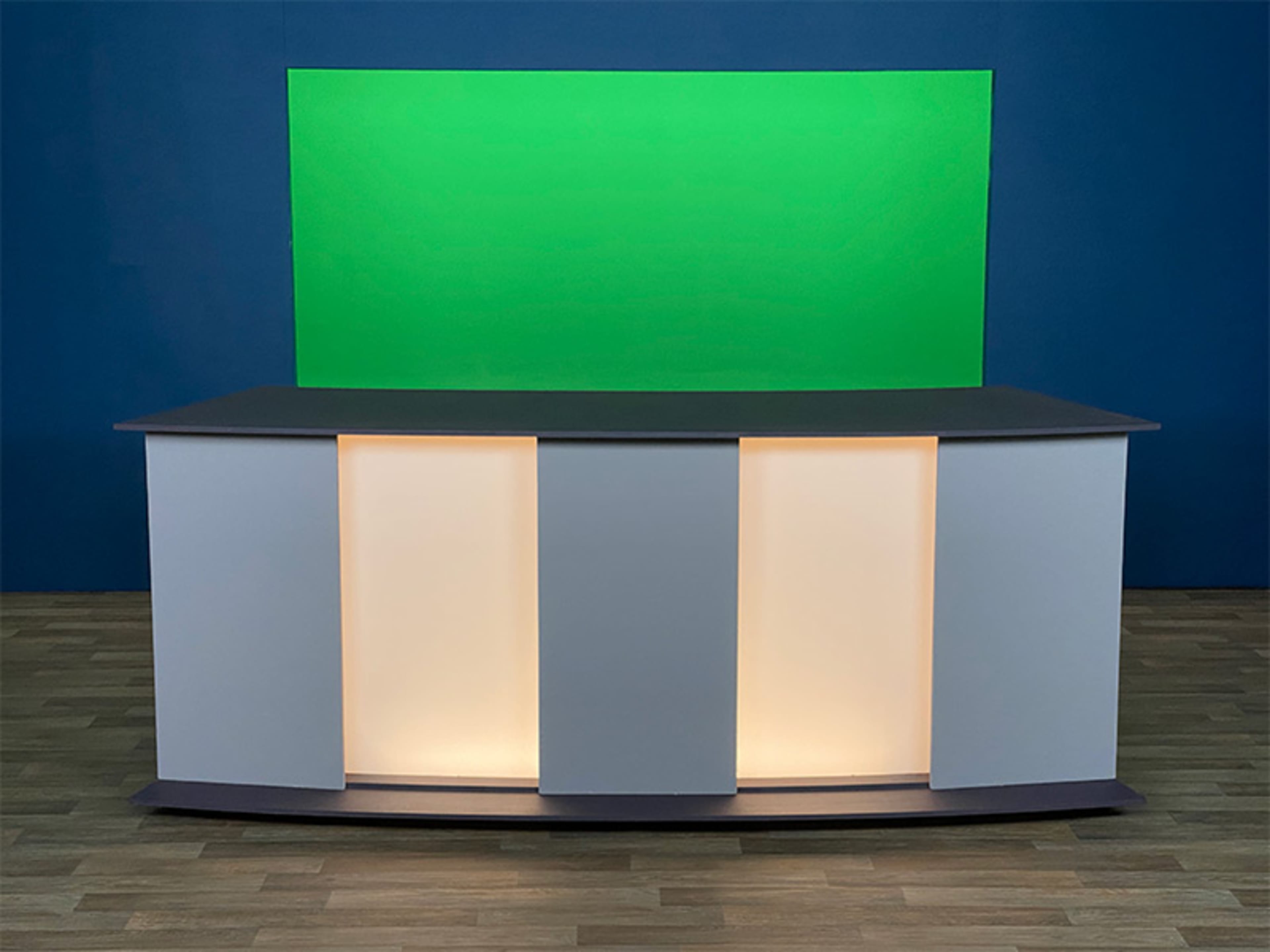 A modern studio set features a gray countertop with illuminated panels and a green backdrop.