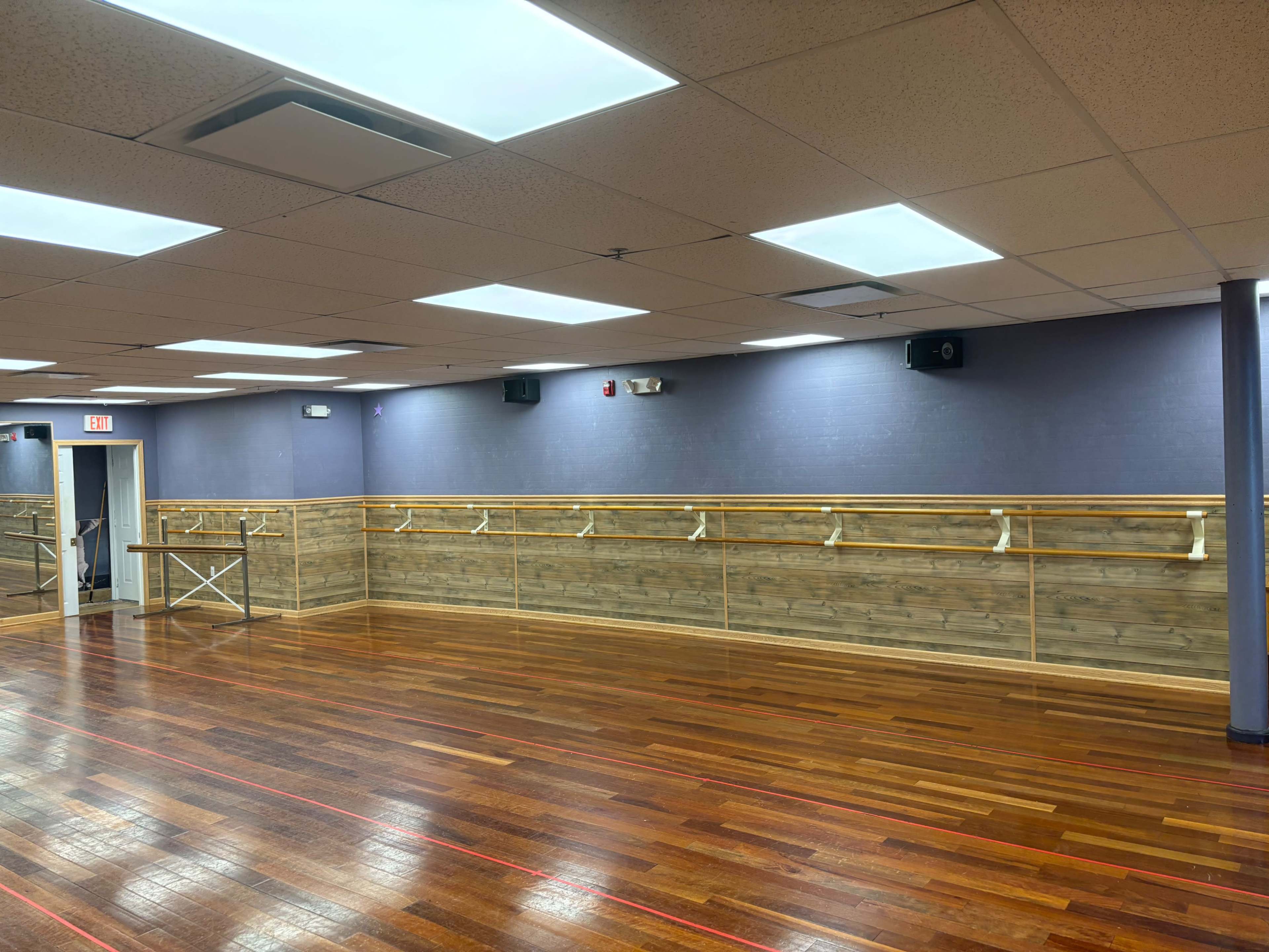 A spacious dance studio with wooden floors, mirrored walls, and ballet barres along one side.