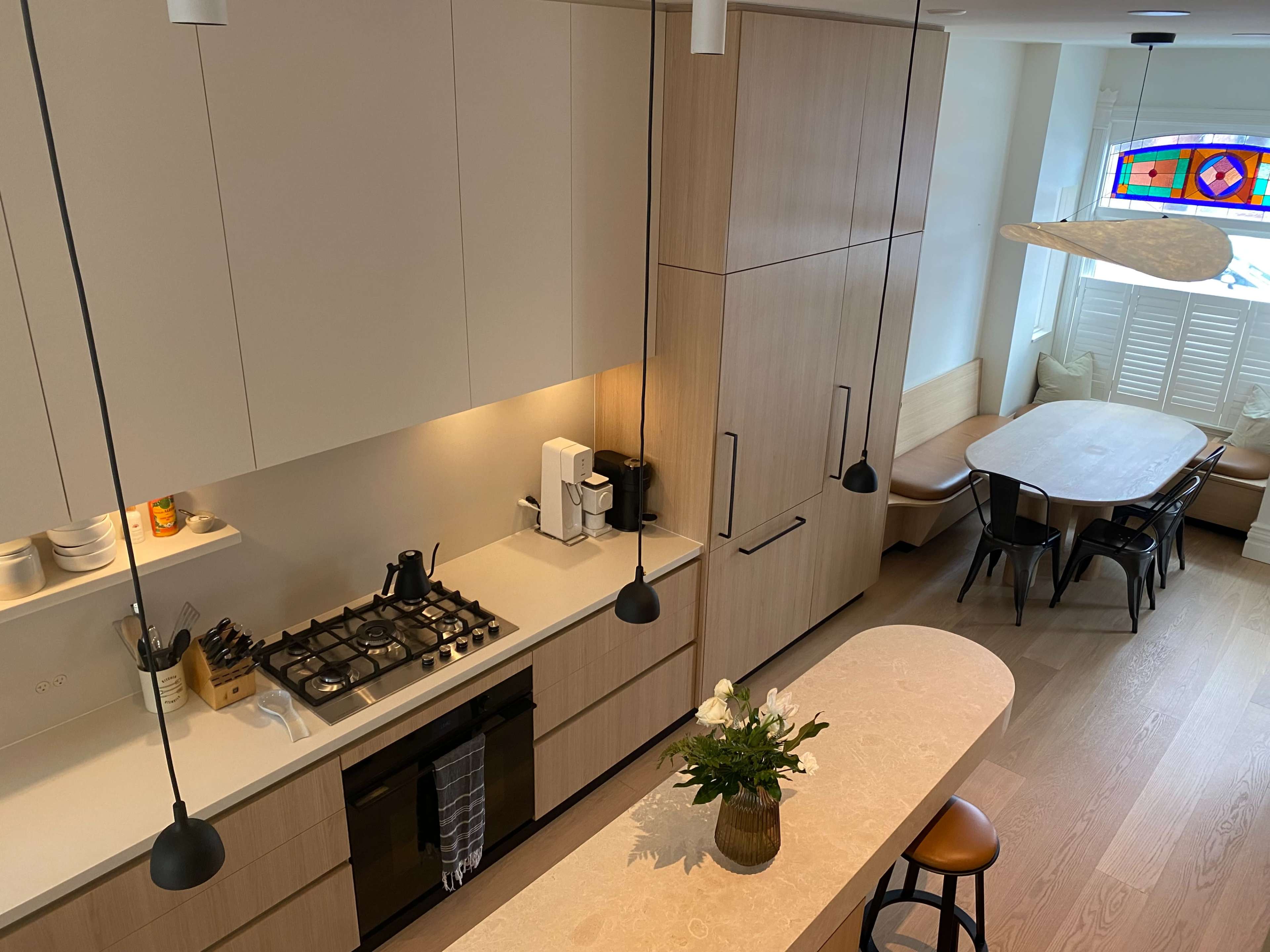A modern kitchen with wooden cabinets, a gas stove, and a dining area featuring a large table and a colorful stained glass window.