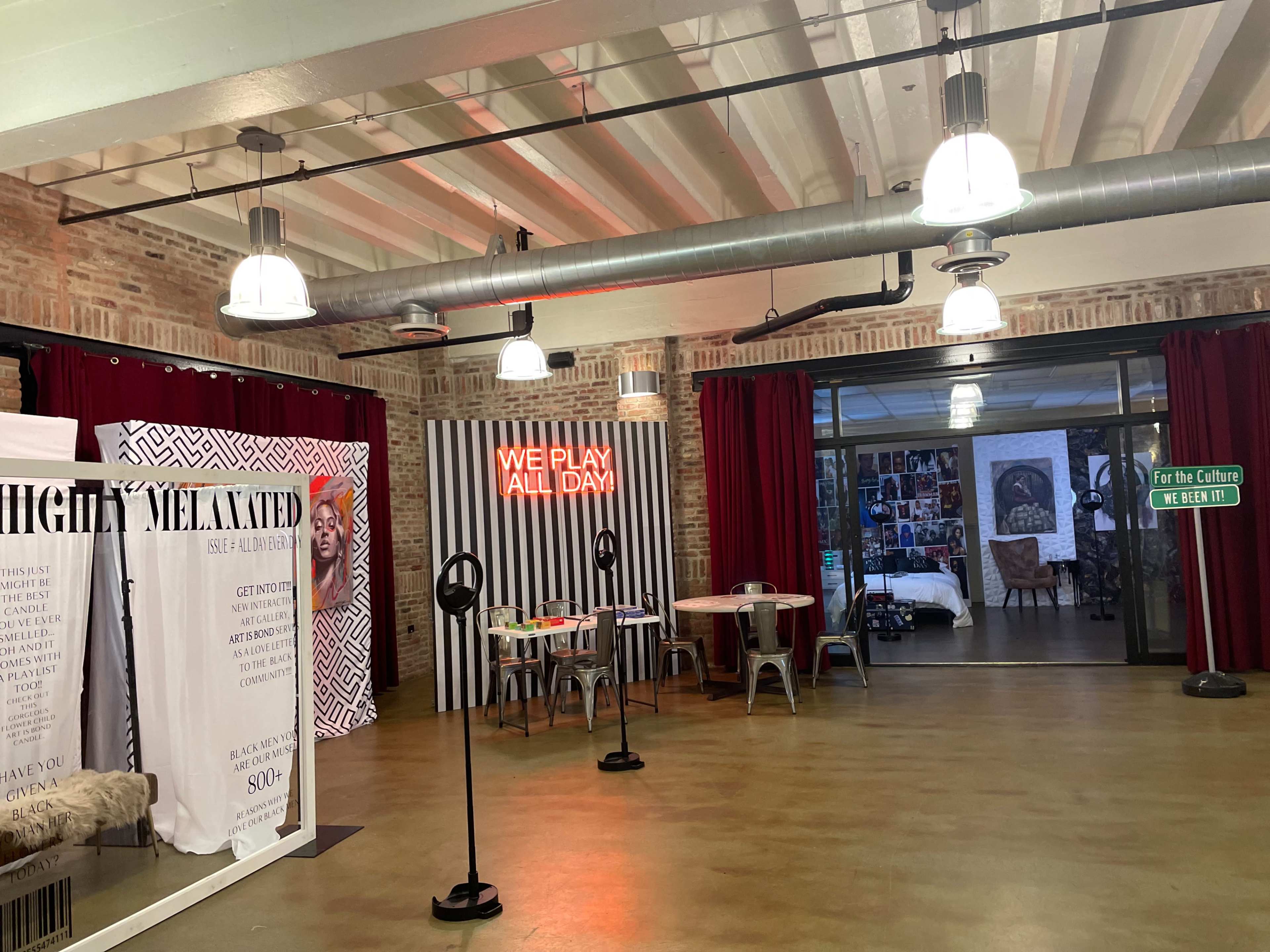 An interior space featuring brick walls, industrial lighting, red curtains, and a mix of seating areas with decorative elements and text displays.