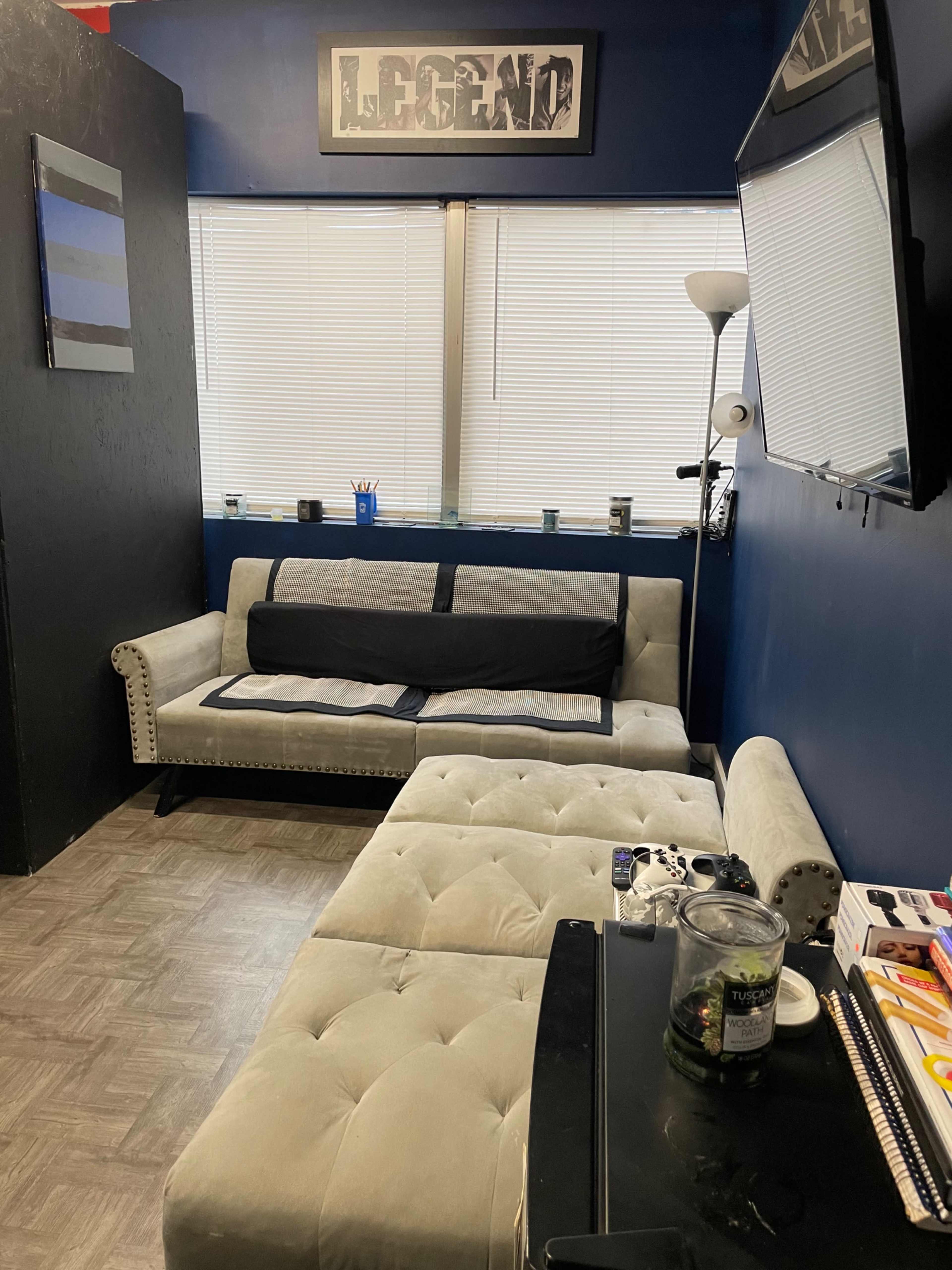 A small room with a gray sectional sofa, a black coffee table, a television mounted on the wall, and posters or decorations on the walls.