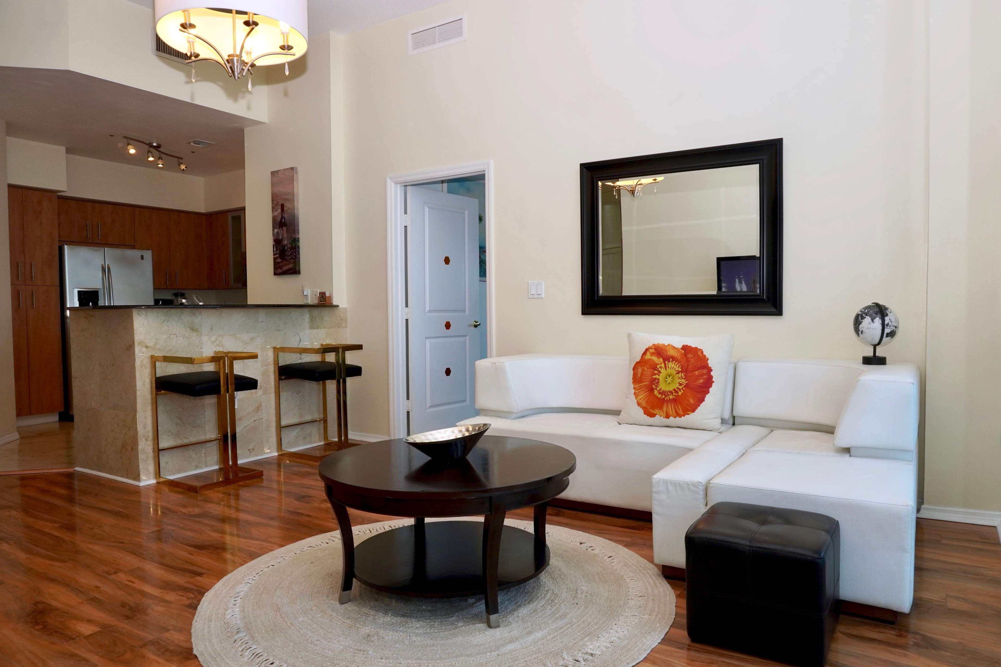 A modern living room with a white sectional sofa, a round coffee table, and a bar area with two stools in the background.
