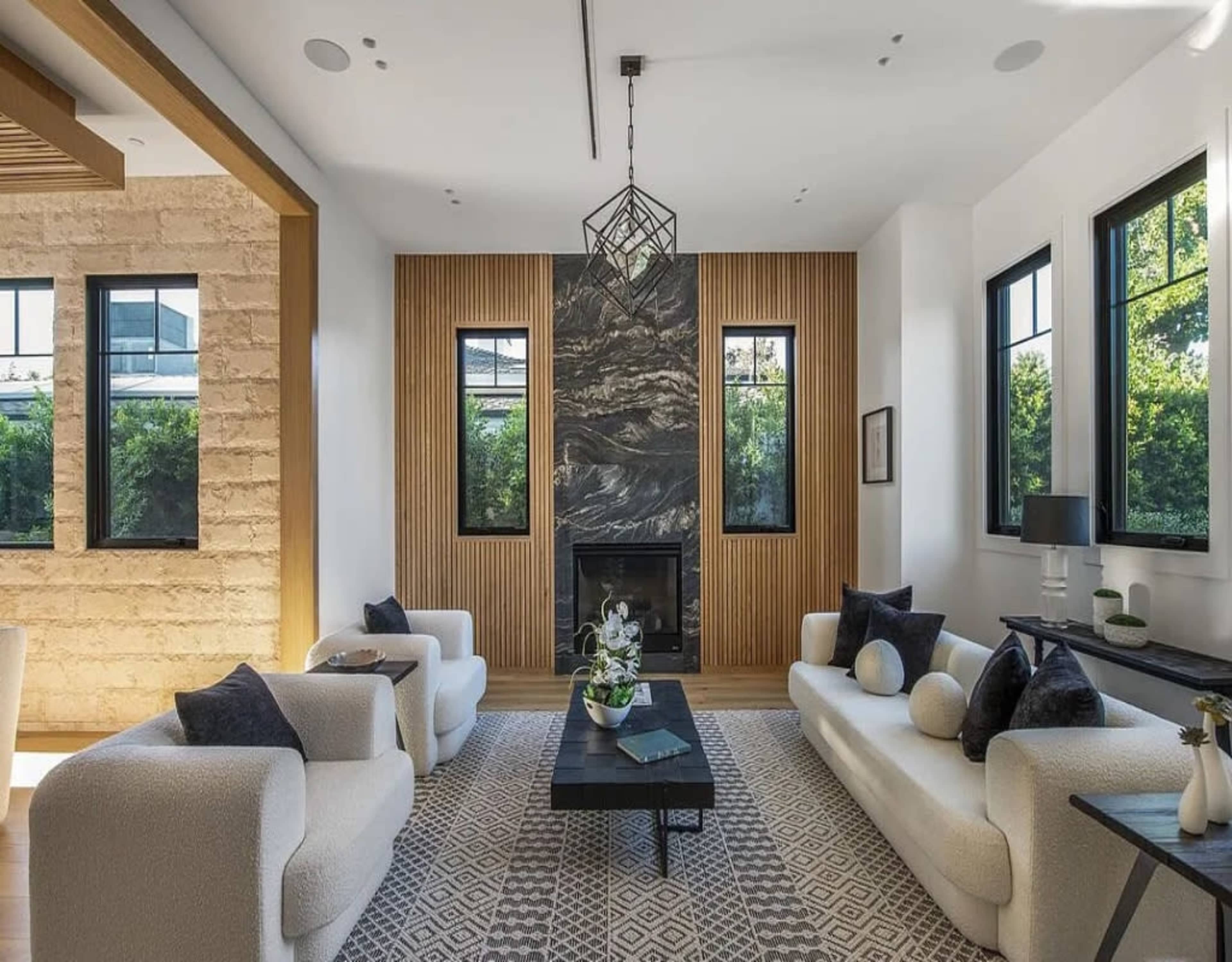 A modern living room features a symmetrical arrangement of plush white sofas facing a dark coffee table, set against a wall with decorative wooden slats and a fireplace.
