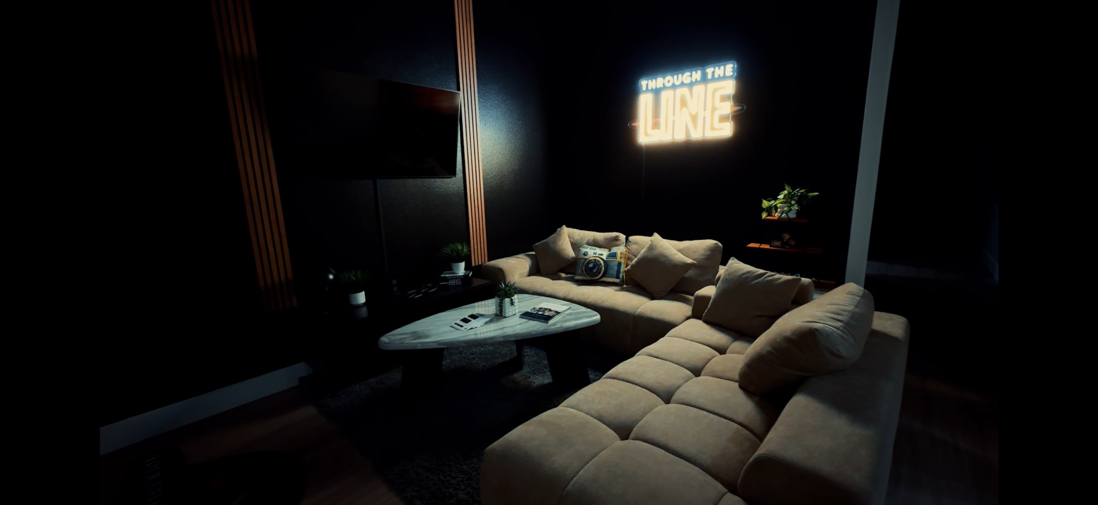 A cozy living room features a large beige sectional sofa, a marble coffee table, and a neon sign that reads "through the line" against a dark wall.