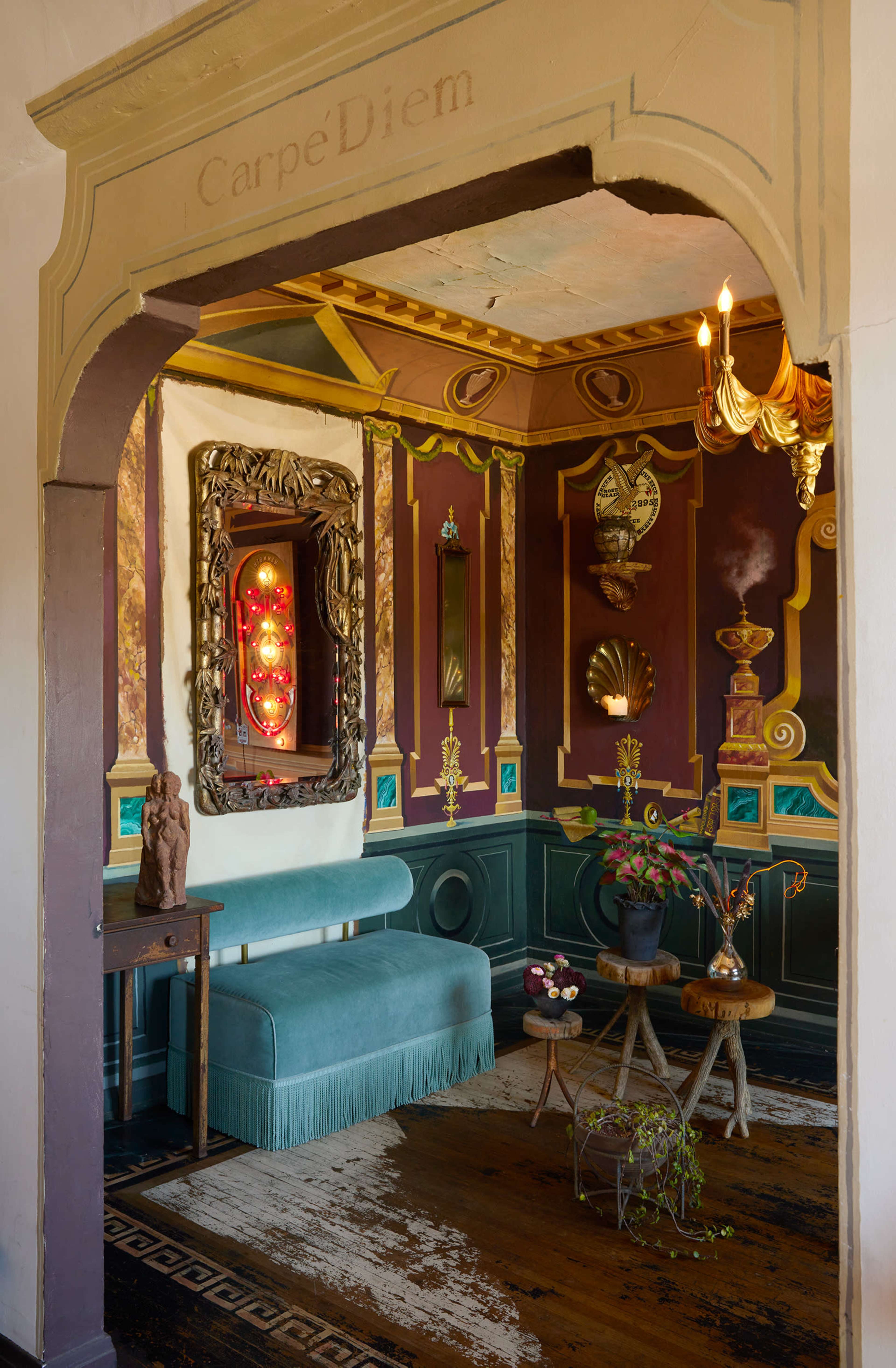 The image shows an ornate room with colorful walls, a blue velvet sofa, and decorative elements like mirrors, clocks, and a chandelier.