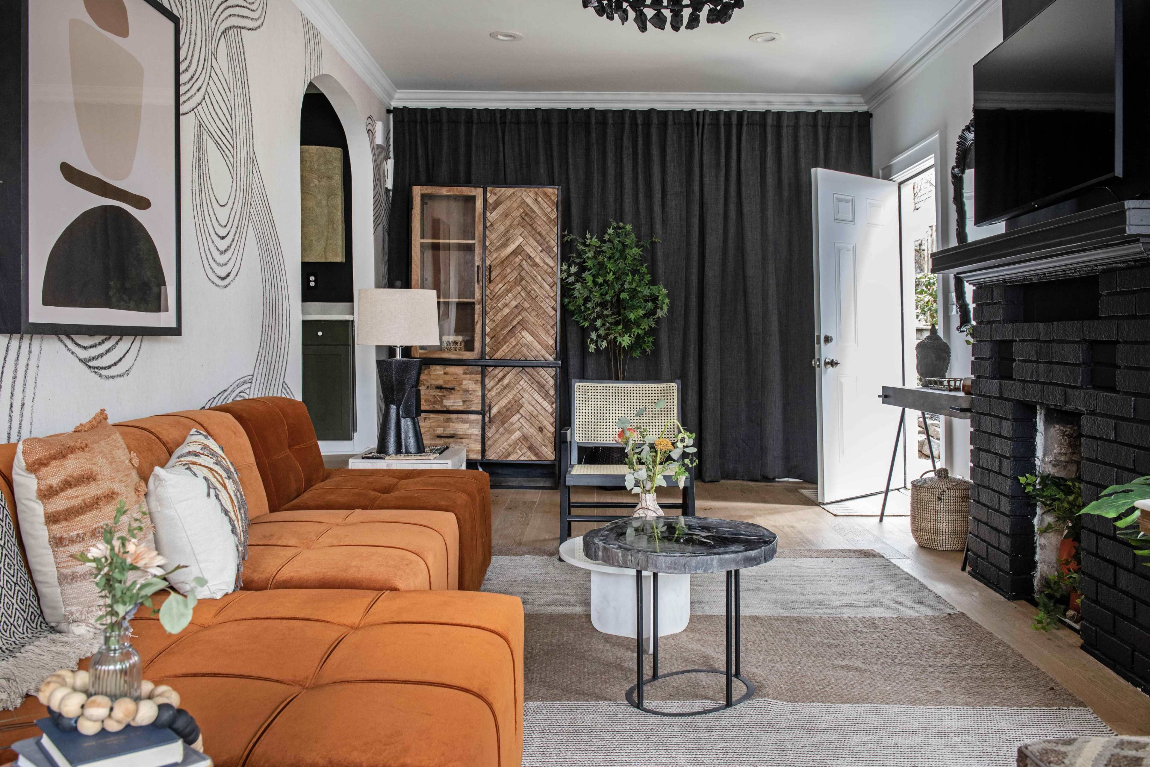 A modern living room features an orange couch, a round coffee table, dark curtains, and a mix of decorative elements including a potted plant and wall art.