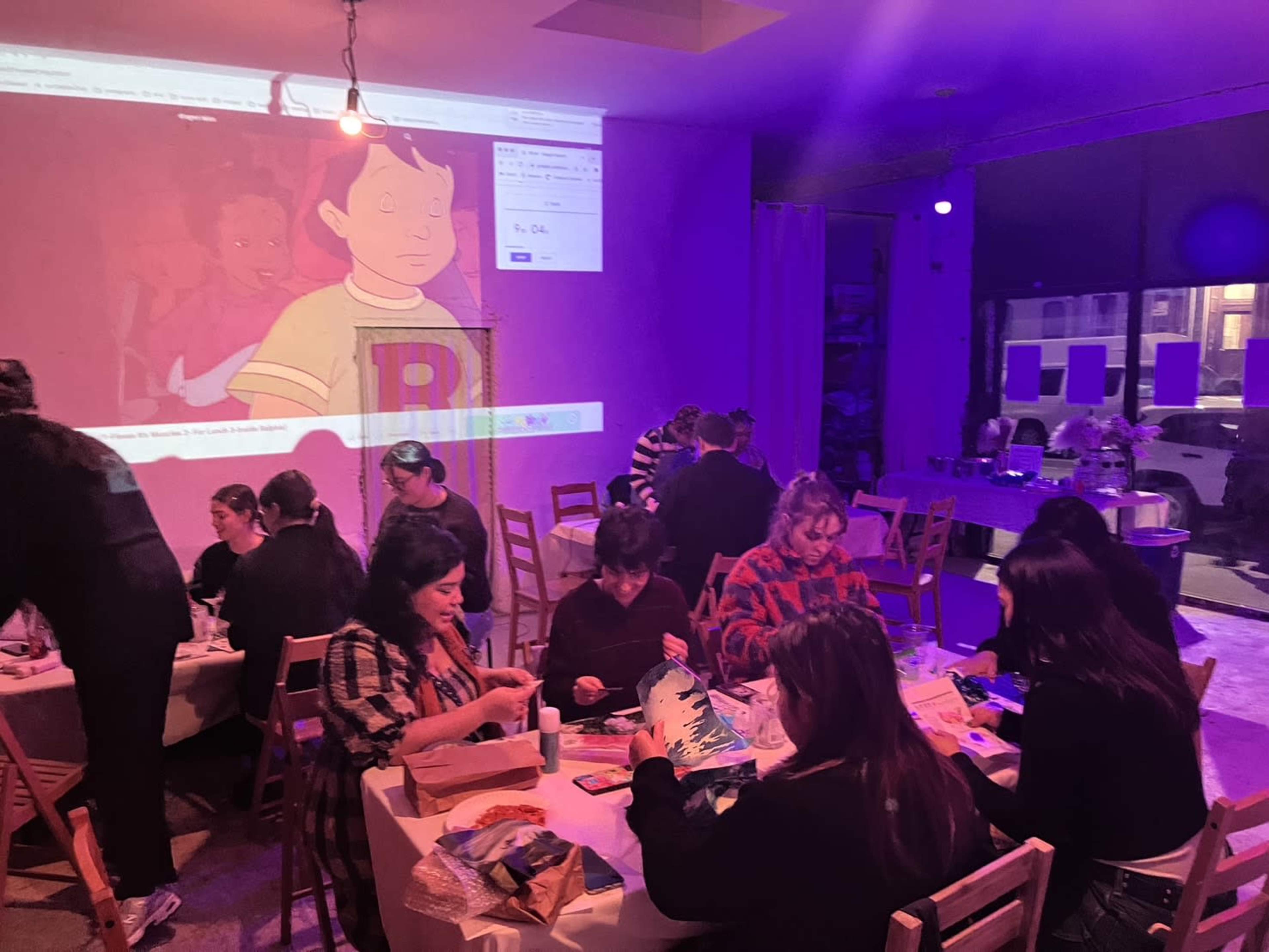 People are gathered around tables, engaging in a creative activity while a character from an animated show is projected on a wall.