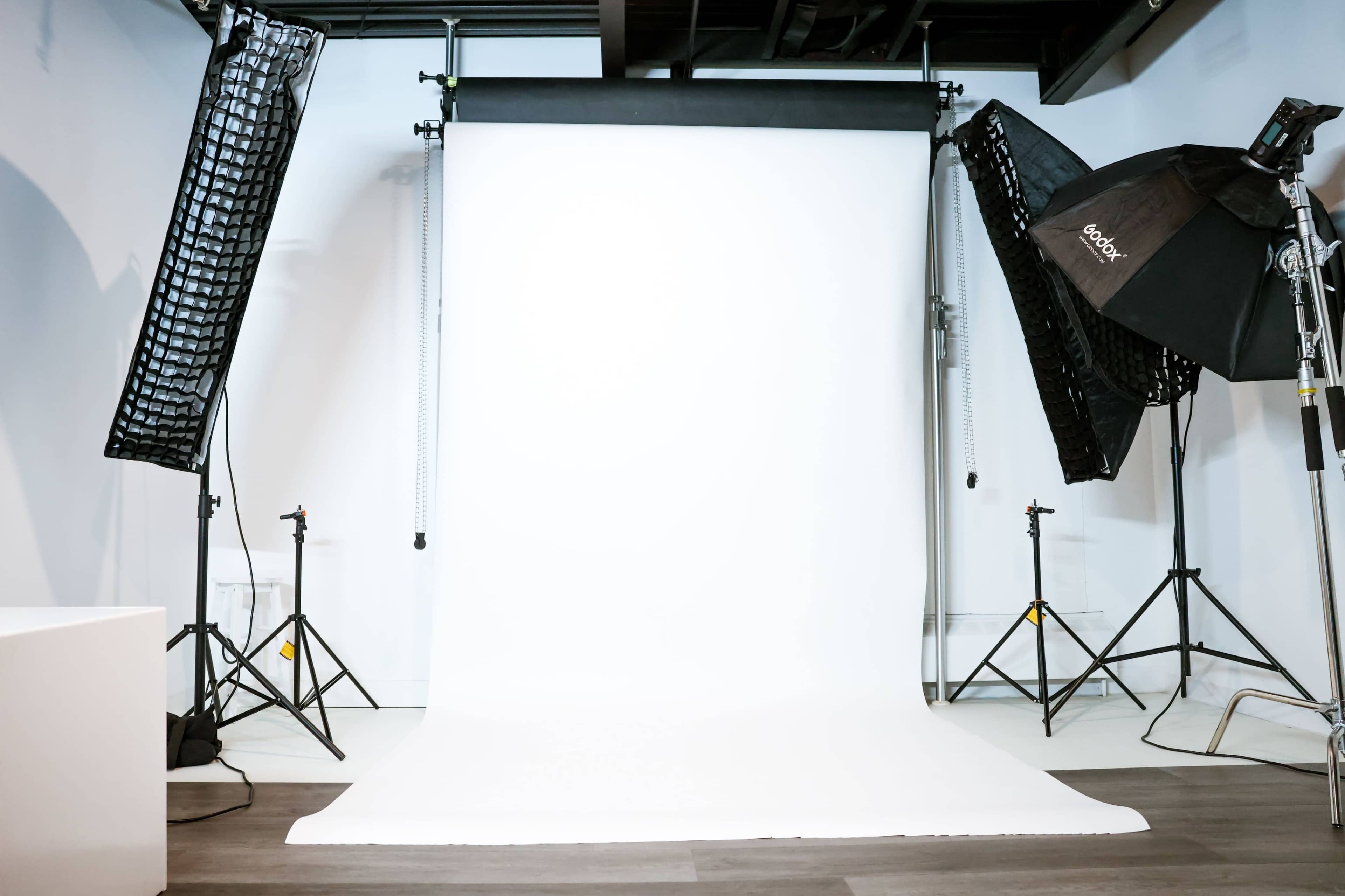 The image shows a photography studio with a white backdrop set up between two light stands and softboxes.