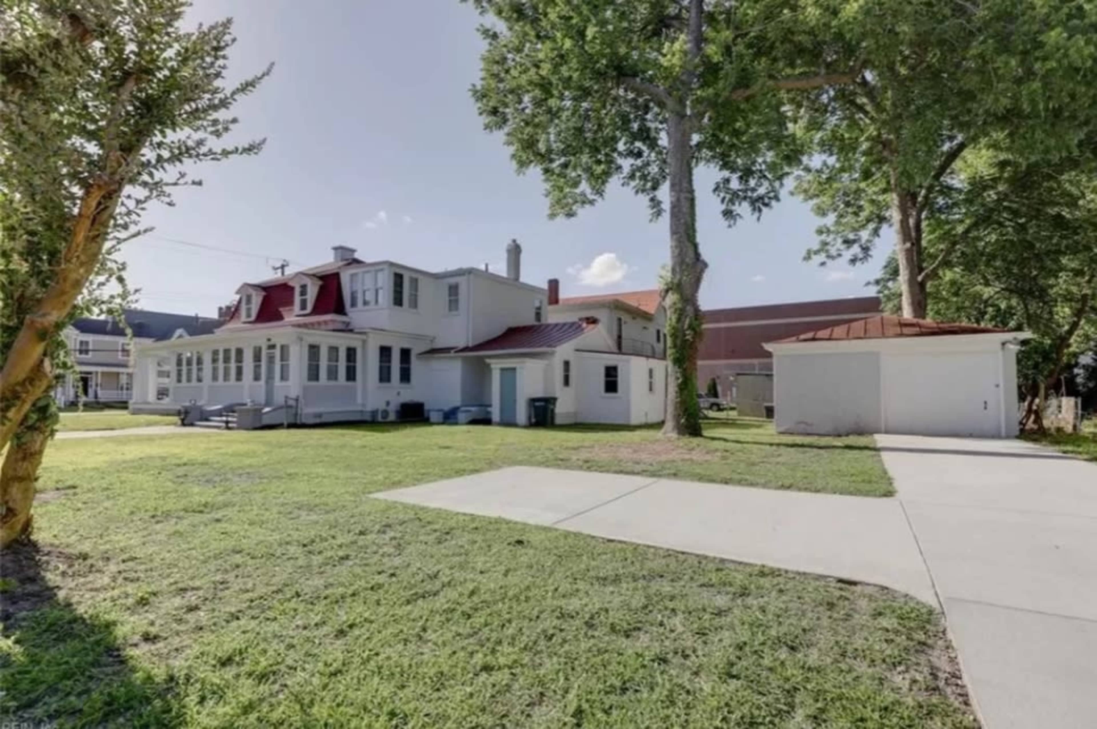 A large, two-story house with a red roof, surrounded by a green lawn and a paved driveway that leads to a detached garage.