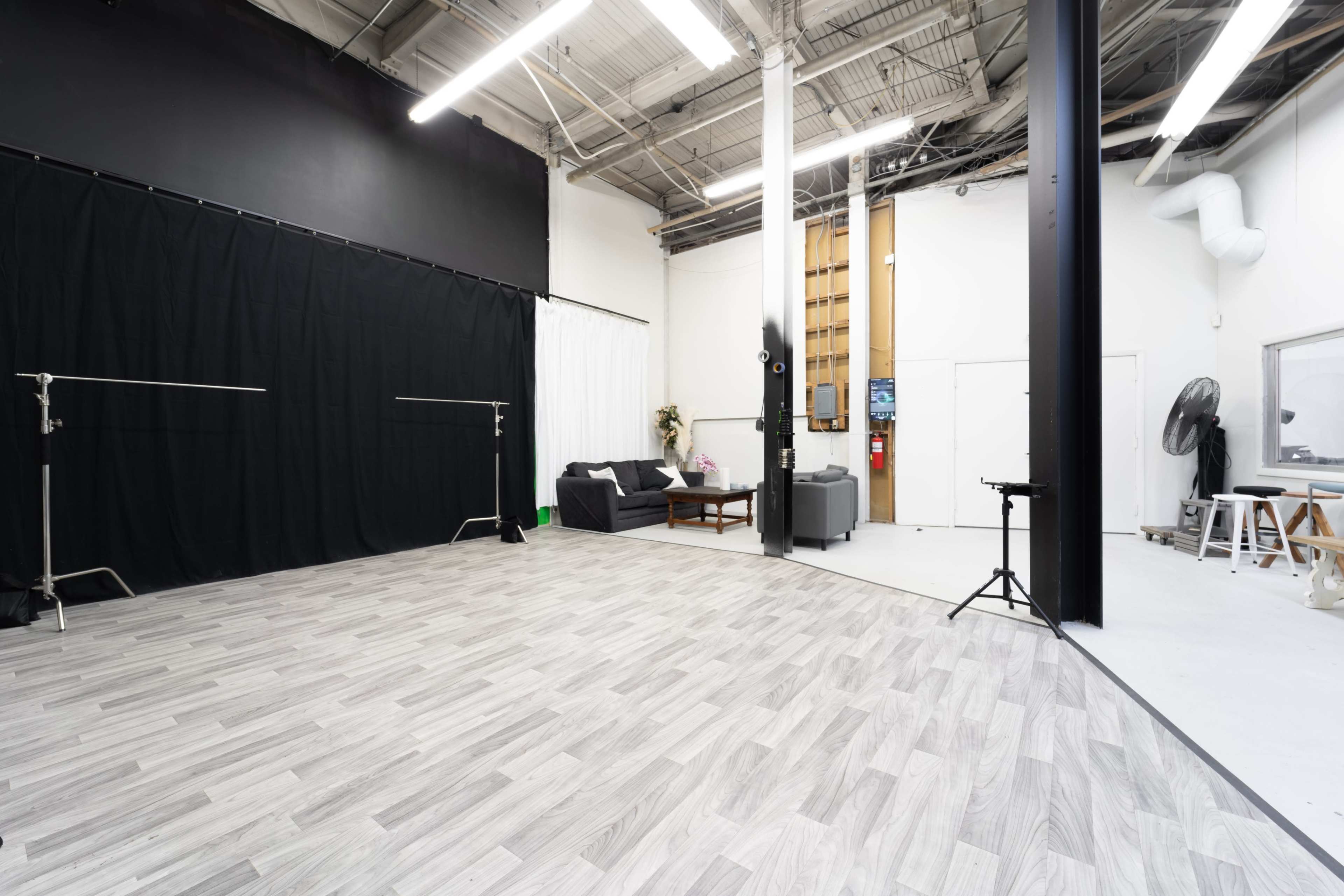 A spacious studio with hardwood floors, black curtains, and seating areas set against white walls.